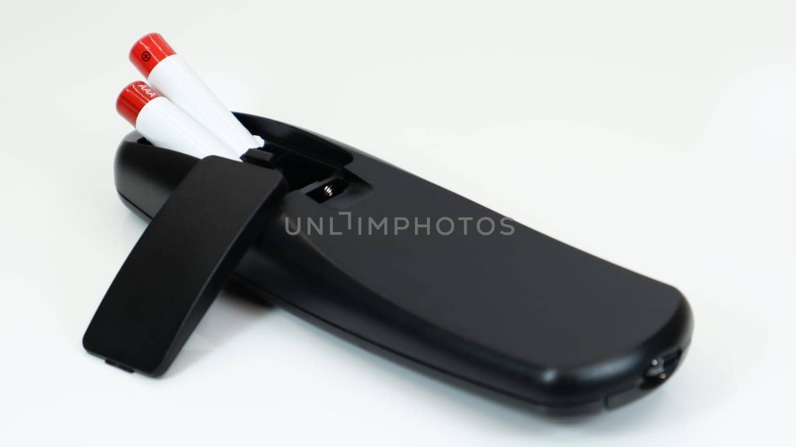 Black TV remote control with AAA alkaline batteries on a white background. Battery replacement, spare parts. Close up of the battery compartment of the remote control