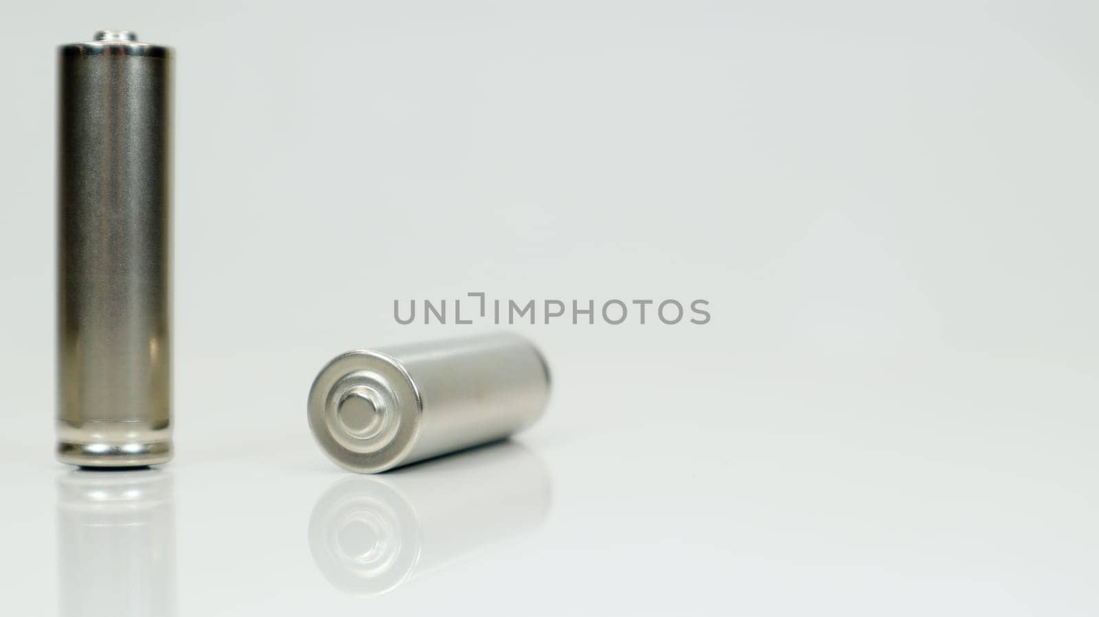 AA alkaline rechargeable batteries on white glossy background with reflection. Close up two empty batteries with copy space