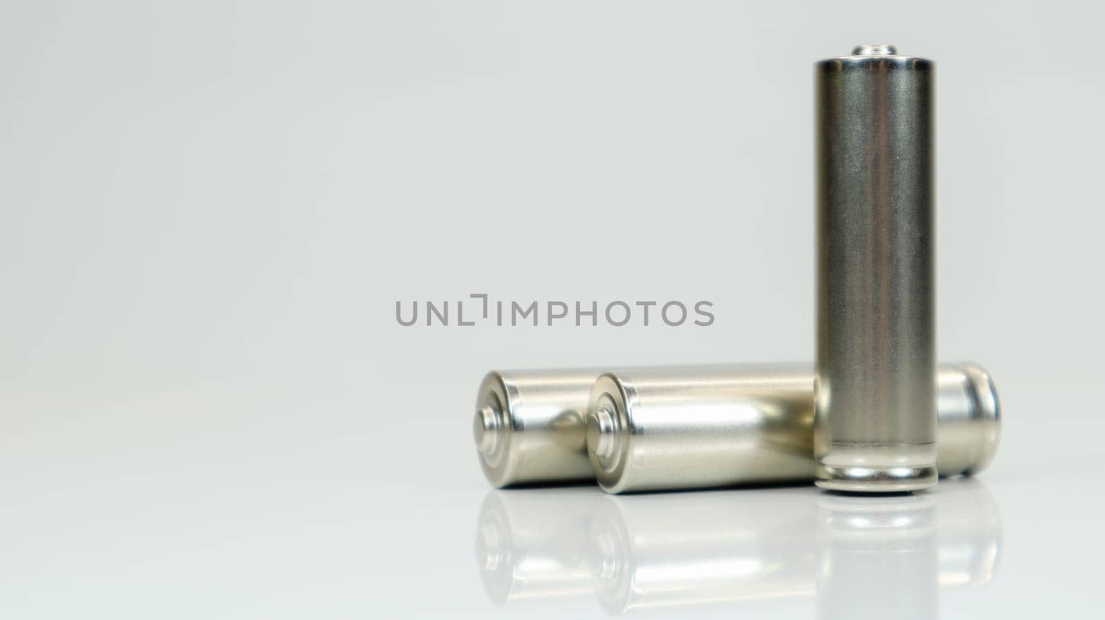 AA alkaline rechargeable batteries on white glossy background with reflection. Close up three empty batteries with copy space