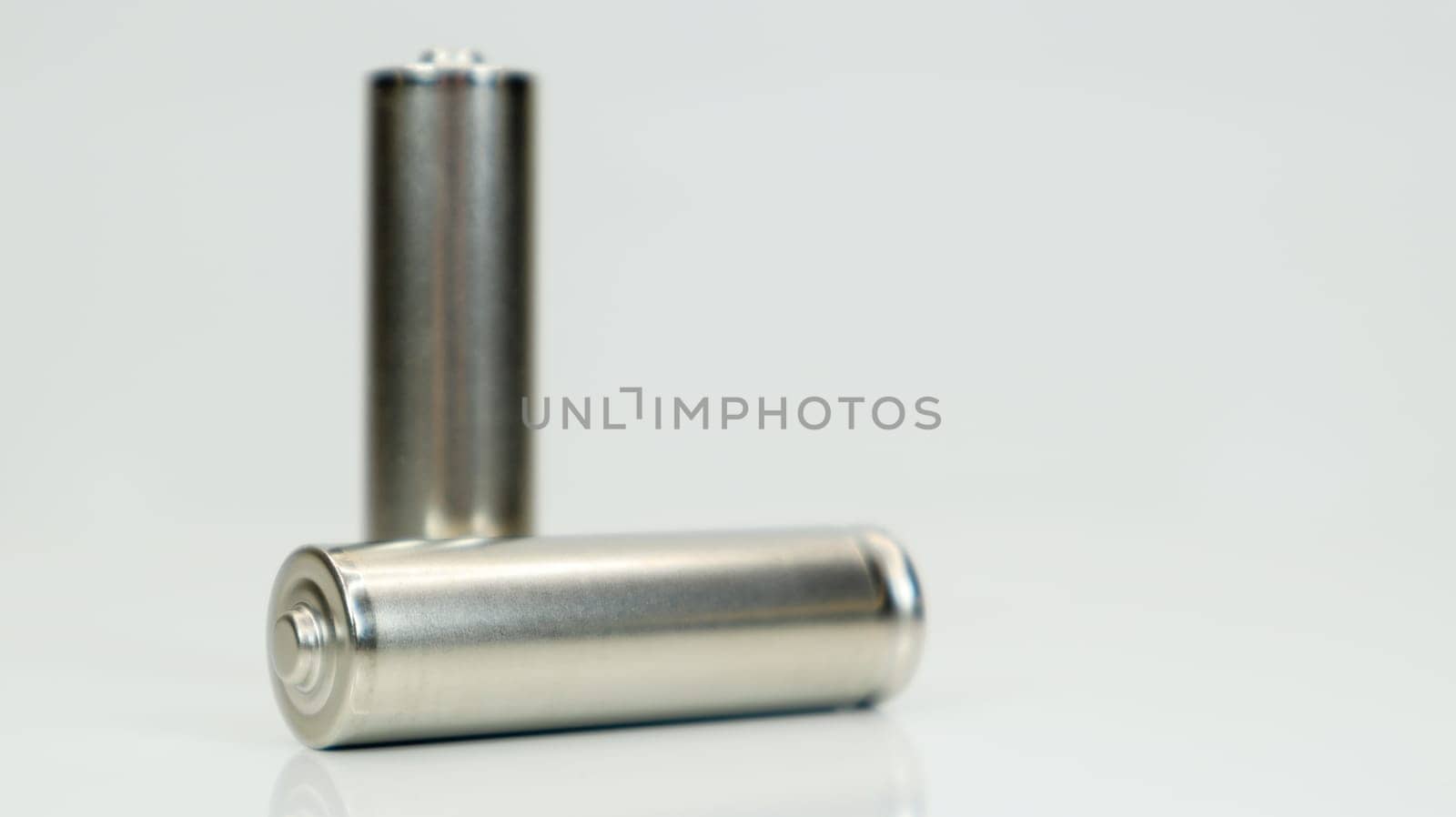 AA alkaline rechargeable batteries on white glossy background with reflection. Close up two empty batteries with copy space