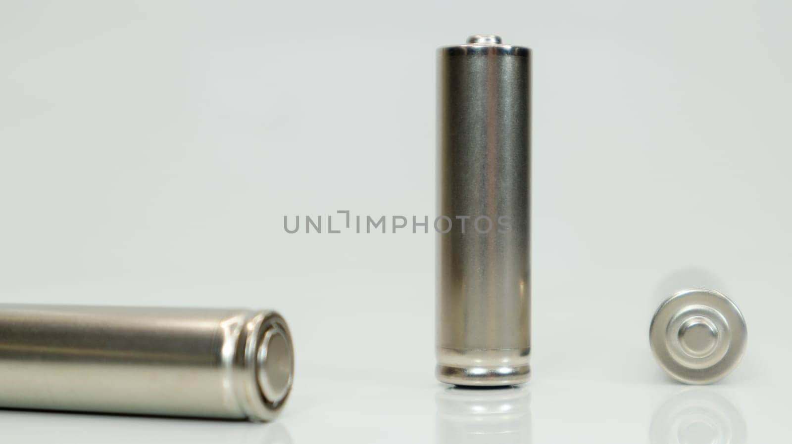 AA alkaline rechargeable batteries on white glossy background with reflection. Close up three empty batteries with copy space