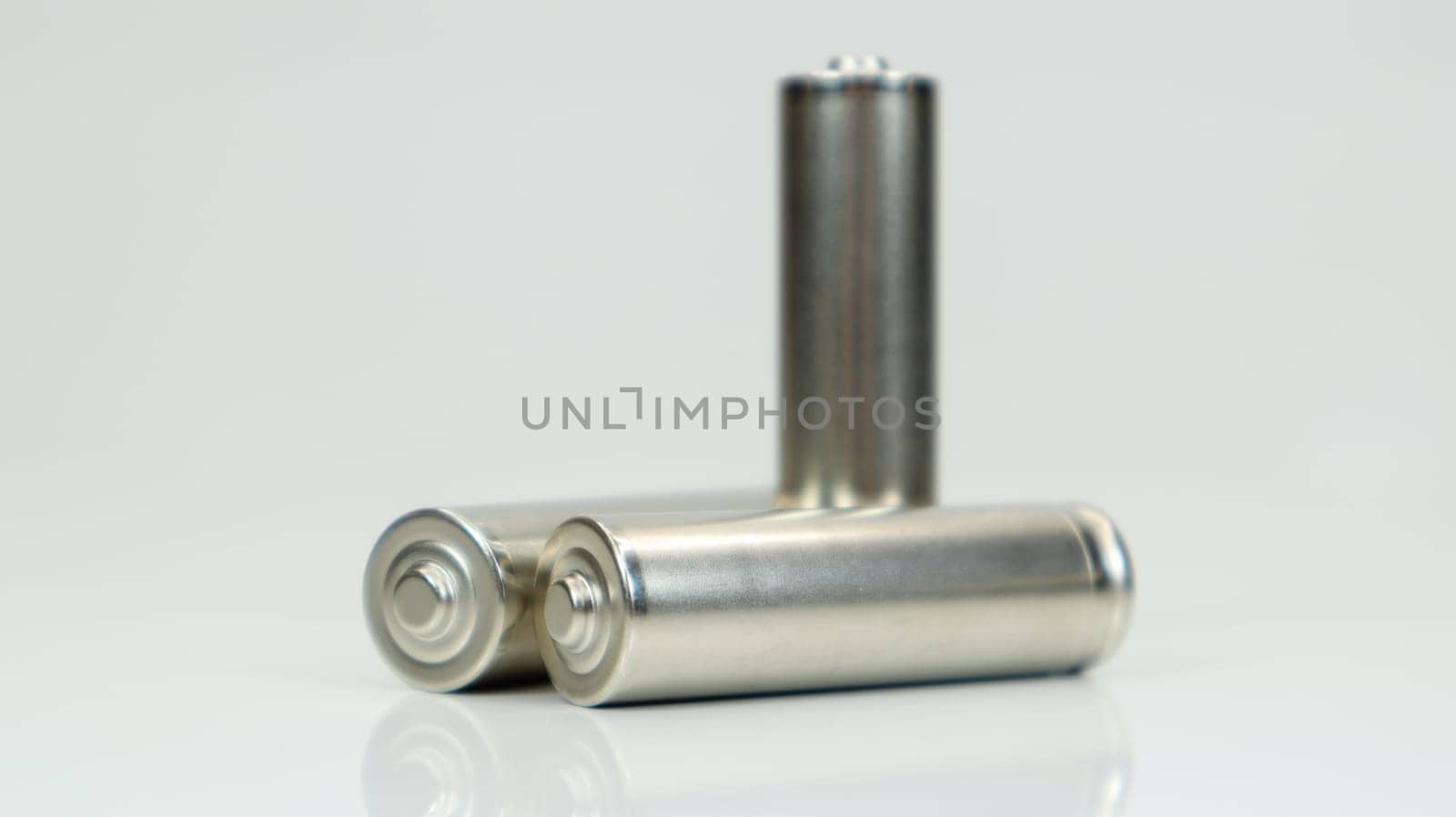 AA alkaline rechargeable batteries on white glossy background with reflection. Close up three empty batteries with copy space