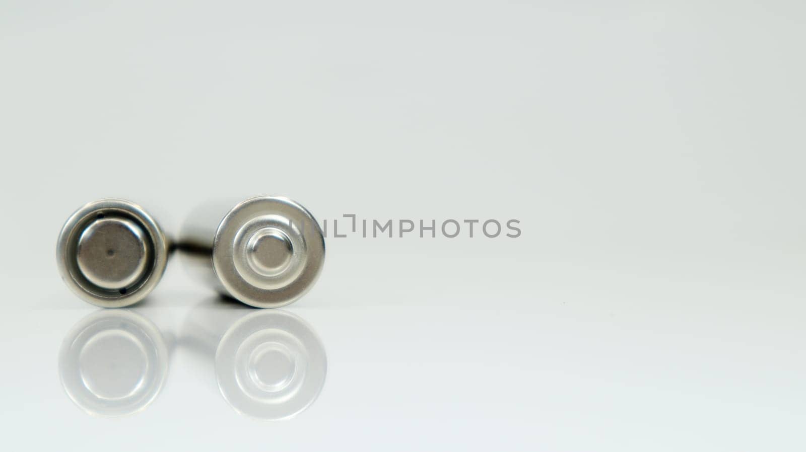 AA alkaline rechargeable batteries on white glossy background with reflection. Close up two empty batteries with copy space