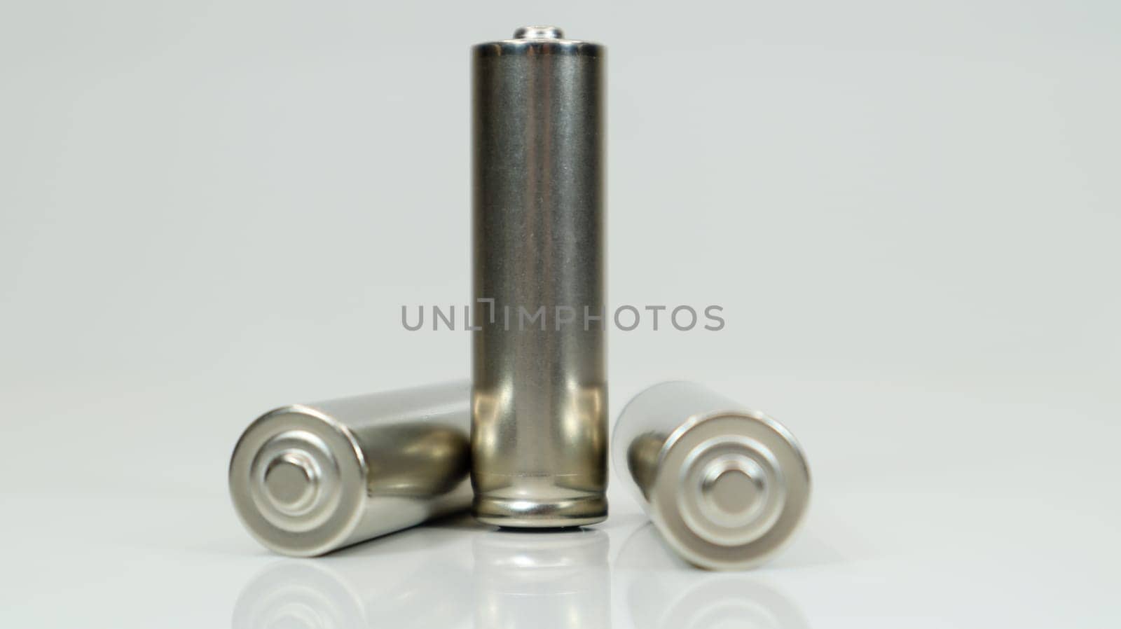 AA alkaline rechargeable batteries on white glossy background with reflection. Close up three empty batteries with copy space