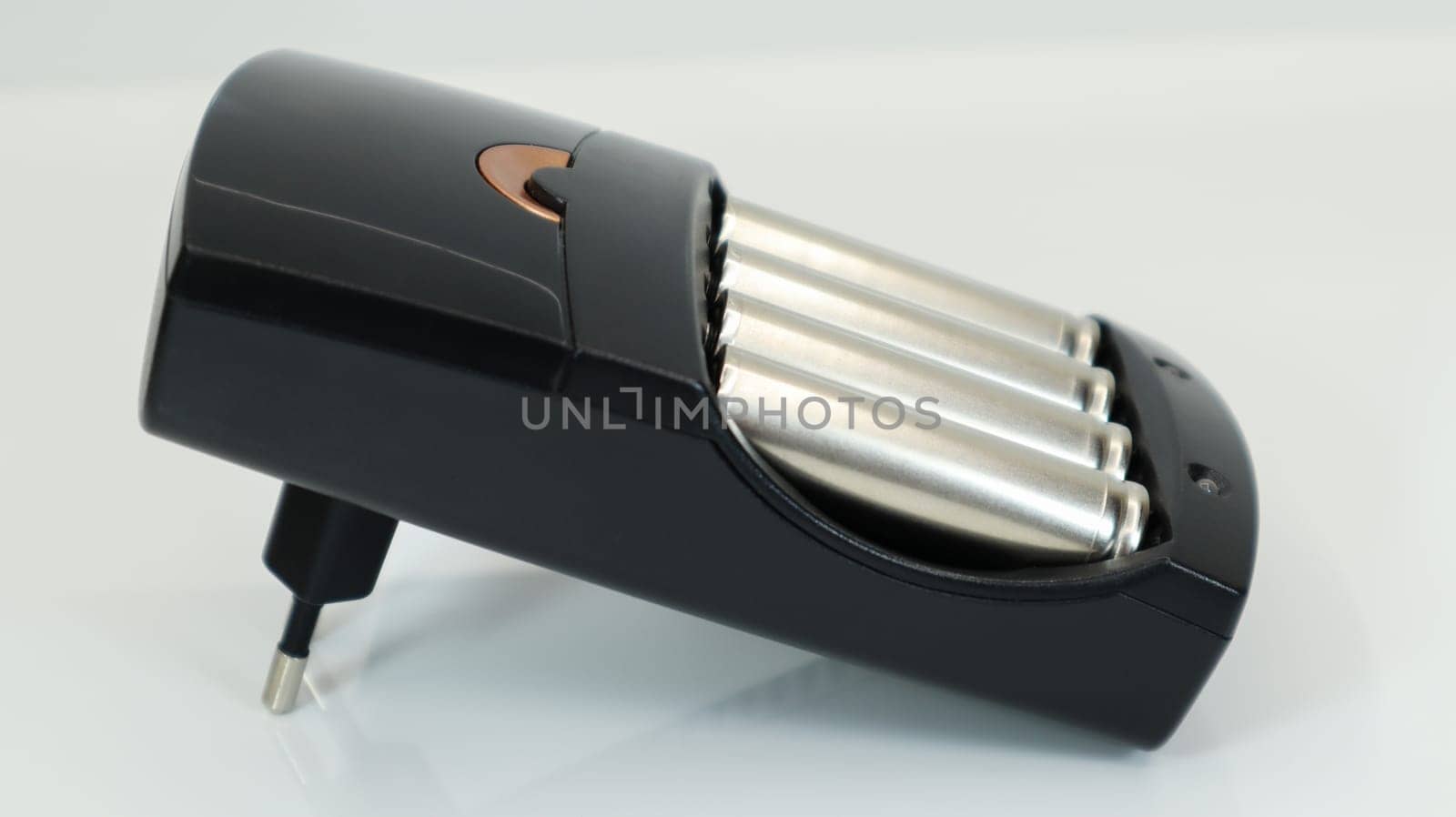 Rechargeable alkaline batteries in a battery charger on a white background. AA fast charger in black. The battery is charging