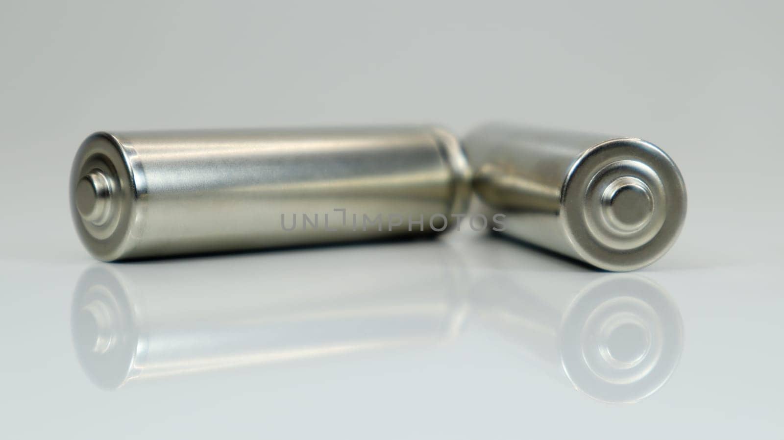 AA alkaline rechargeable batteries on white glossy background with reflection. Close up two empty batteries with copy space