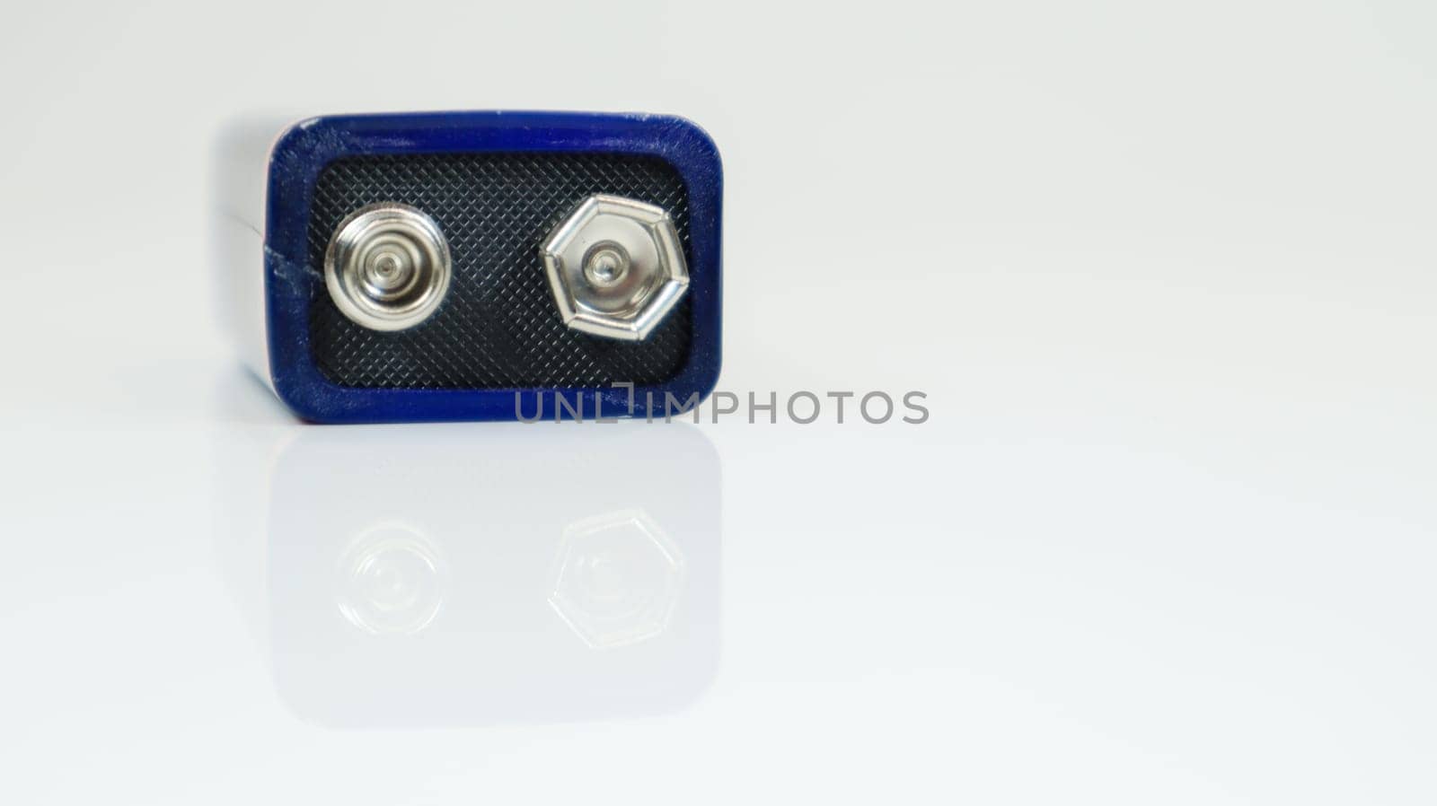 One blue used PP3 battery on a white background with reflection. Main battery for personal power supplies. Close-up of a scratched and used battery connector