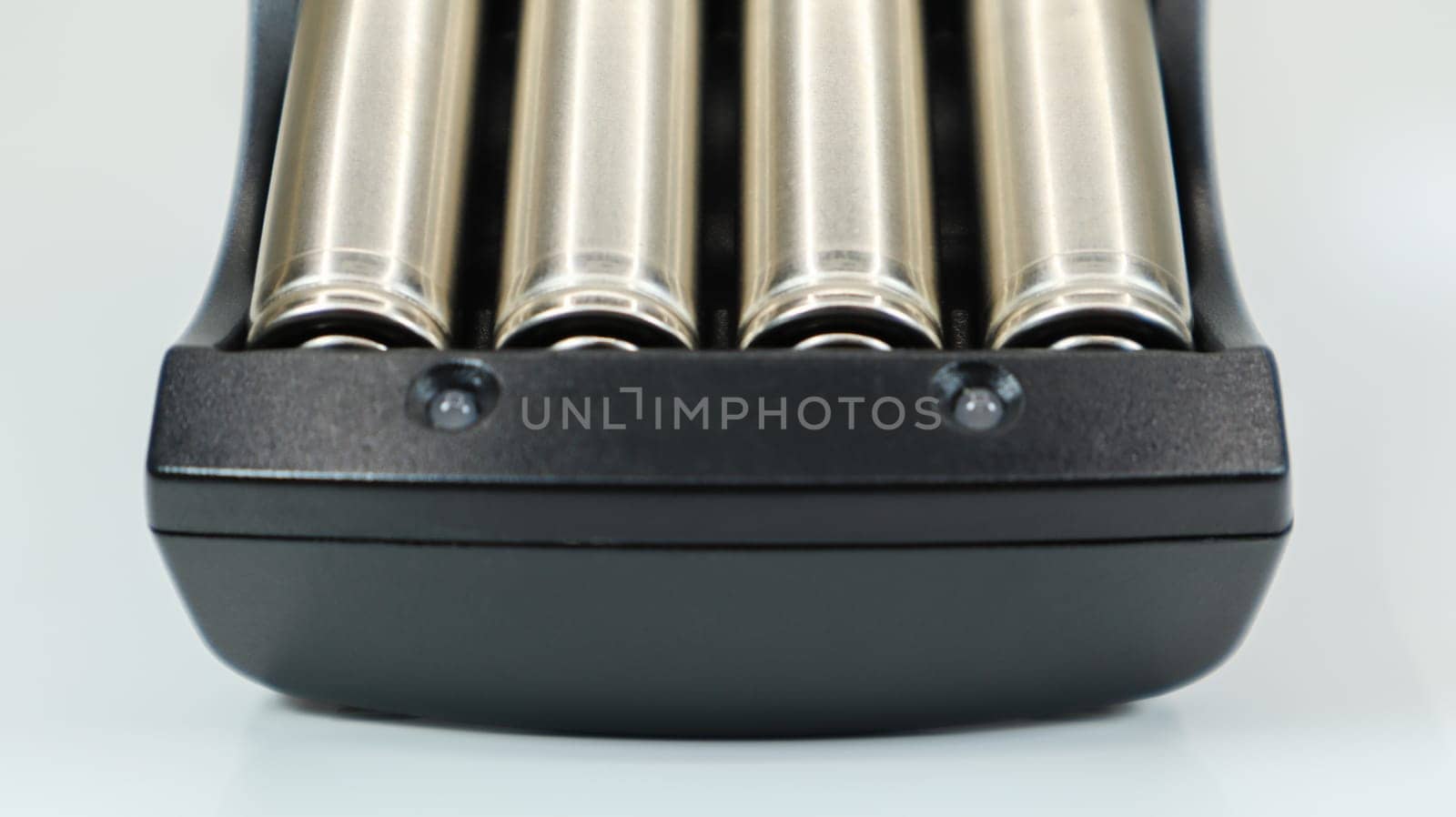 Rechargeable alkaline batteries in a battery charger on a white background. AA fast charger in black. The battery is charging