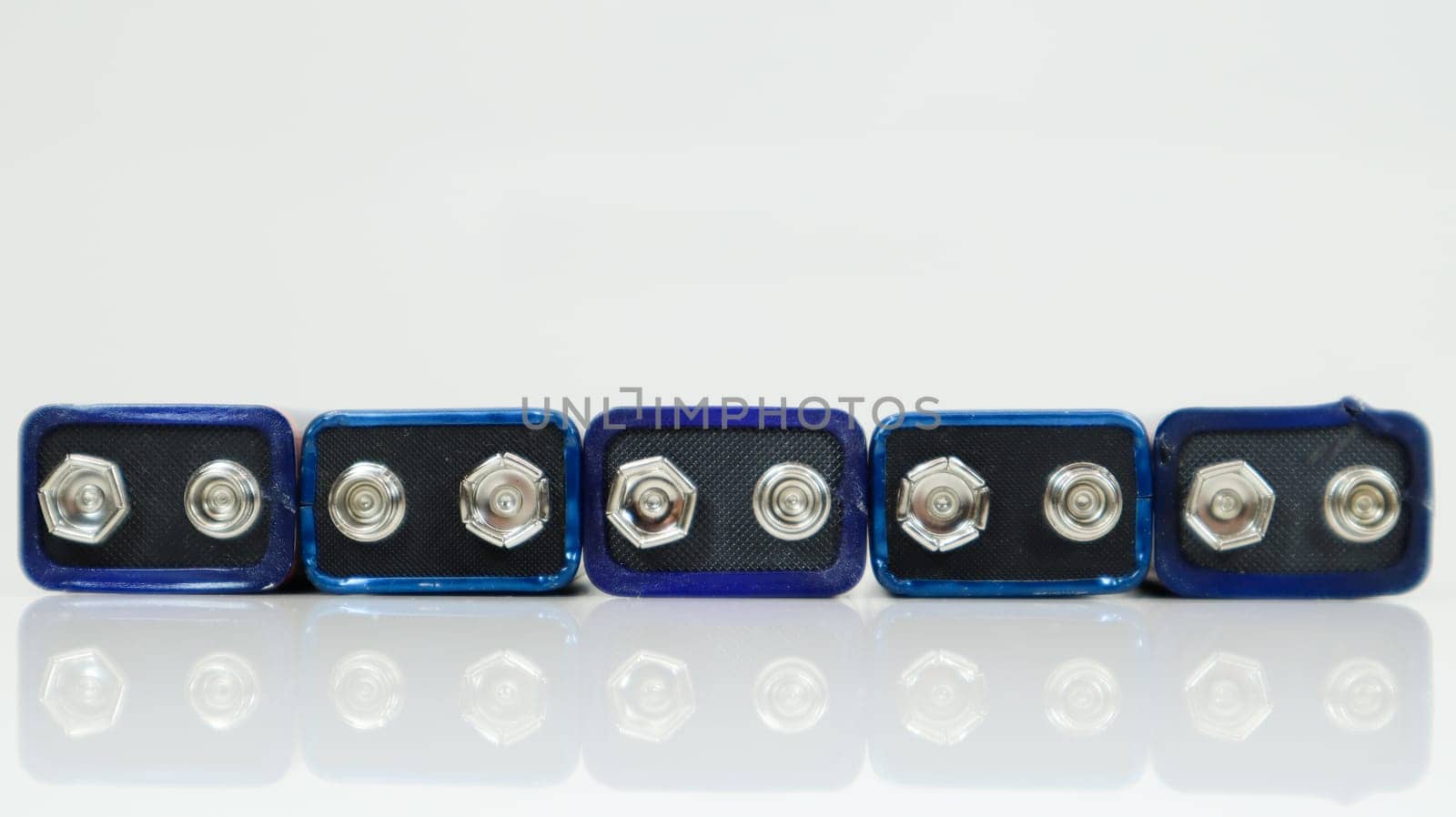 Five blue used PP3 batteries lined up on a white background with reflection. Main battery for personal power supplies. Close-up of a scratched and used battery connector