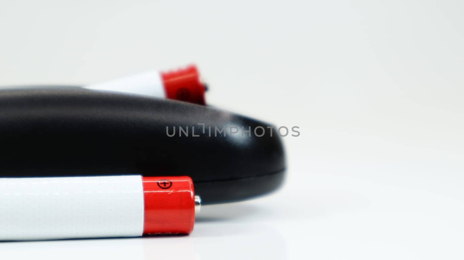 Black TV remote control with AAA alkaline batteries on a white background. Battery replacement, spare parts. Close up of the battery compartment of the remote control
