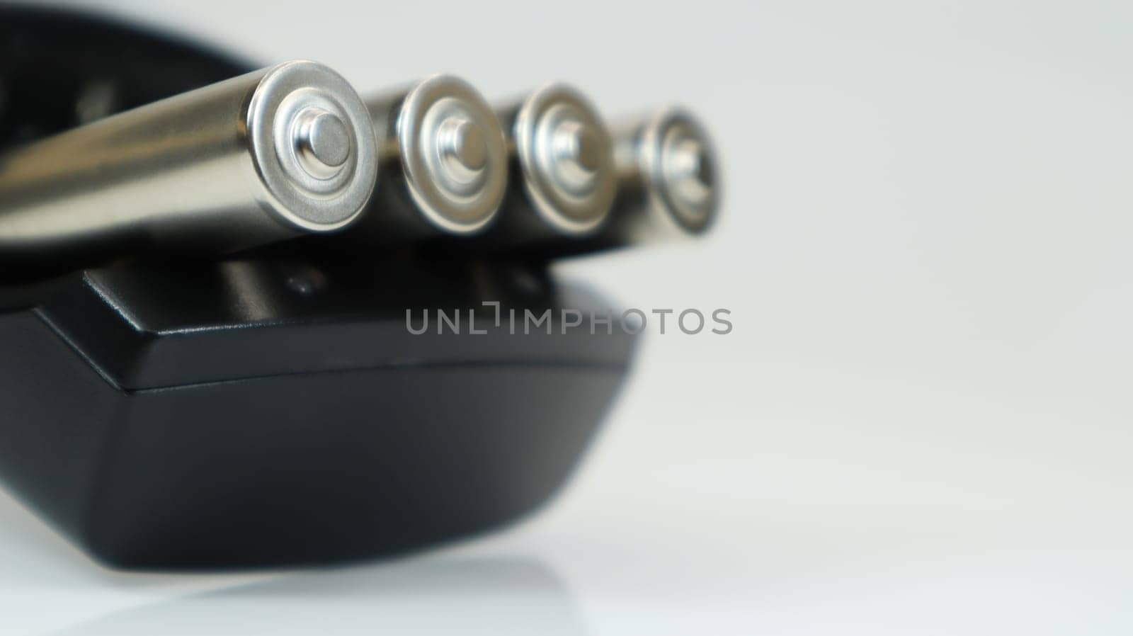 Rechargeable alkaline batteries in a battery charger on a white background. AA fast charger in black. The battery is charging