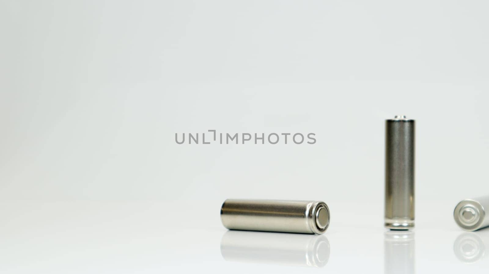 AA alkaline rechargeable batteries on white glossy background with reflection. Close up three empty batteries with copy space