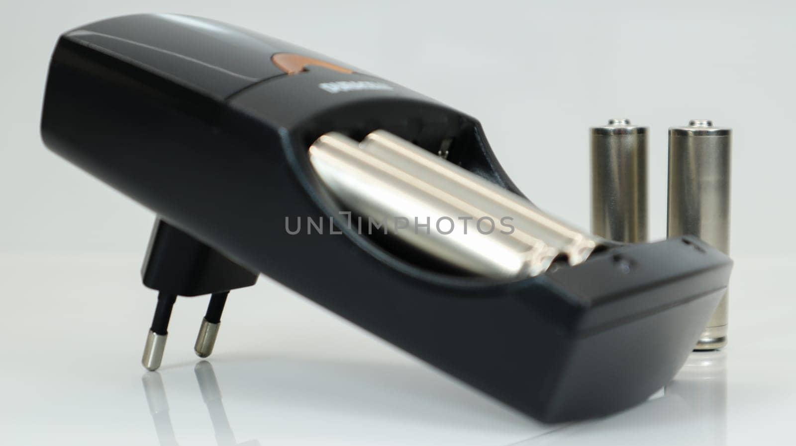 Rechargeable alkaline batteries in a battery charger on a white background. AA fast charger in black. The battery is charging
