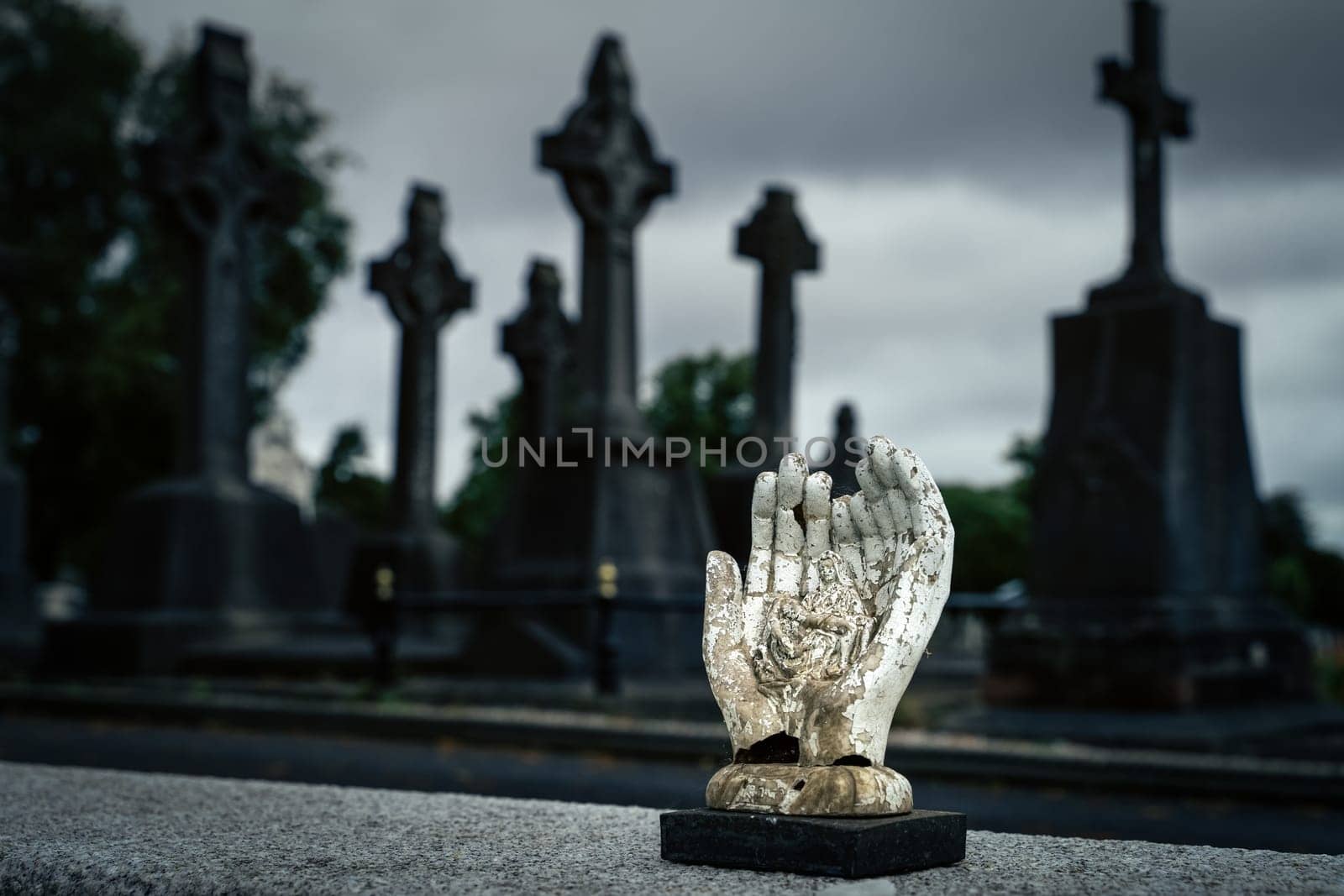 Dublin, Ireland, August 2019 Sculpture of hands holding holly Mary and Jesus Christ with blurred Celtic crosses in Glasnevin Cemetery