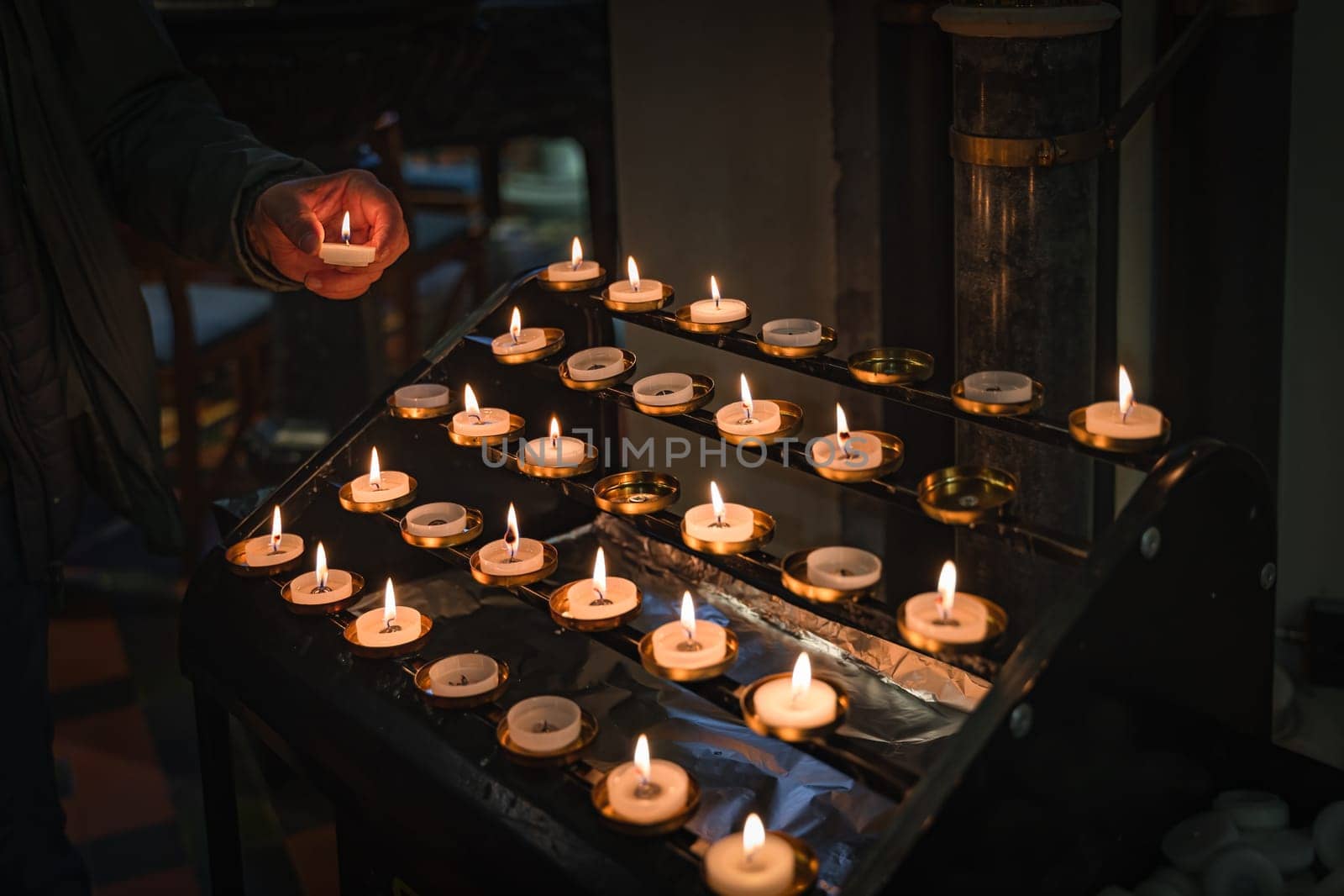 Hand holding a lit candle, putting it on altar. Candles are lit for prayer intentions in places of worship. St Patricks Cathedral, Dublin, Ireland