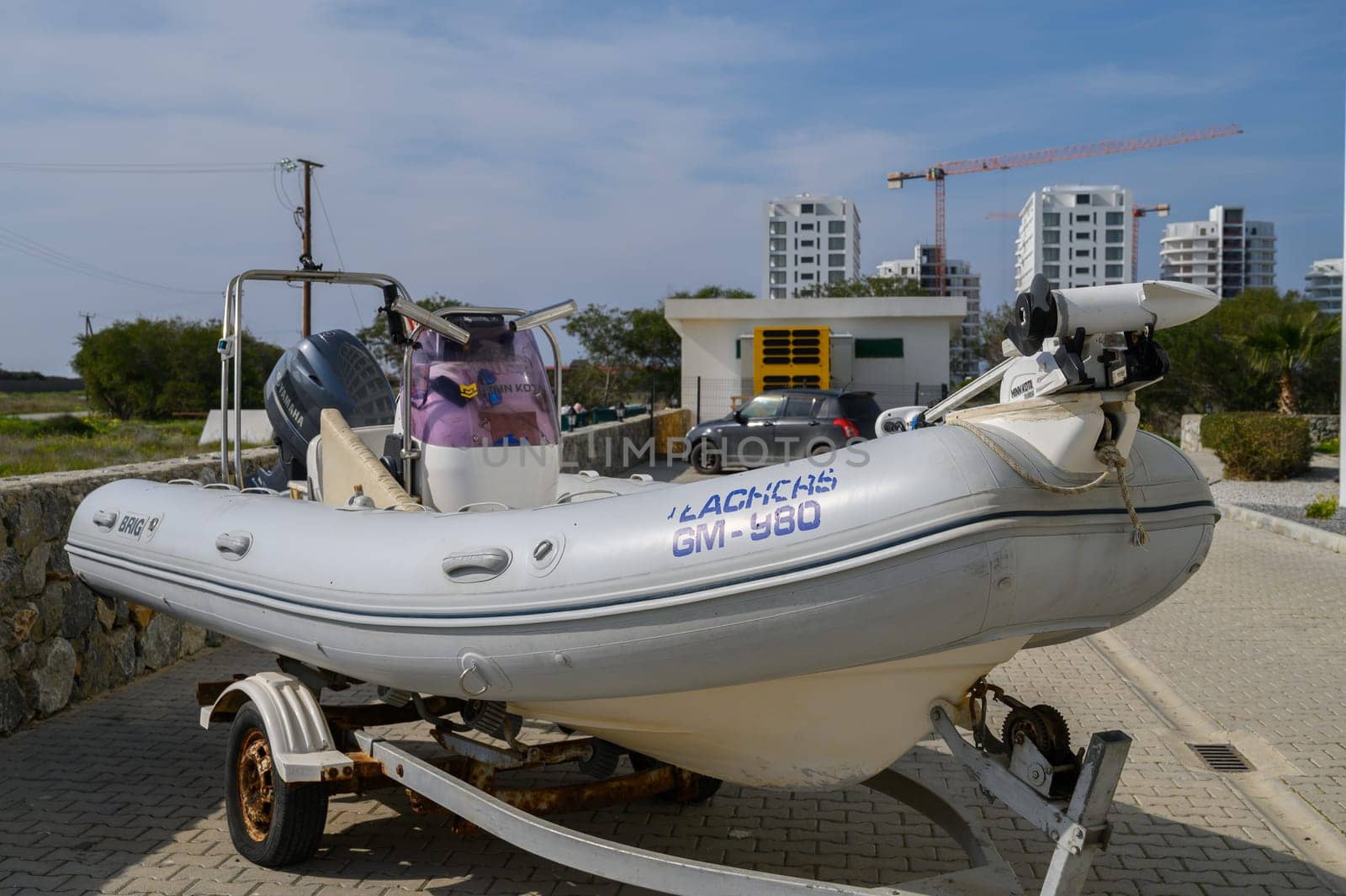 Gaziveren Cyprus -15.02.2025 A small inflatable boat rests on a trailer by the waterfront under a bright sky, surrounded by modern buildings.