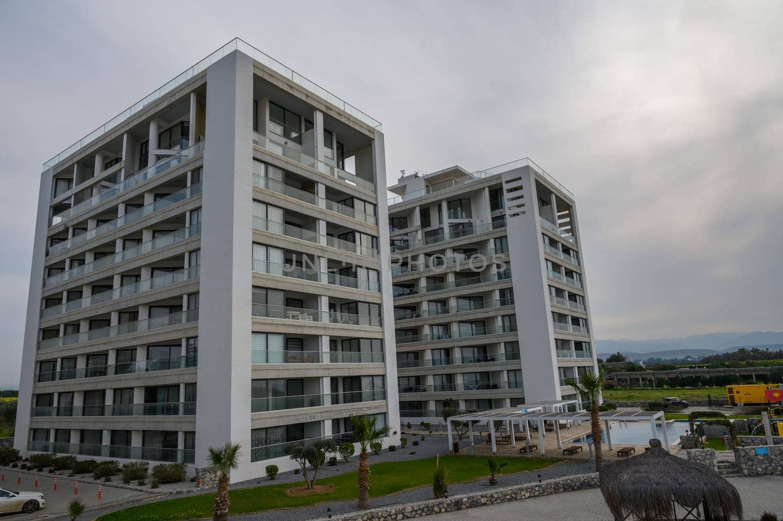 Two modern buildings tower over a serene area with palm trees and outdoor amenities nearby.