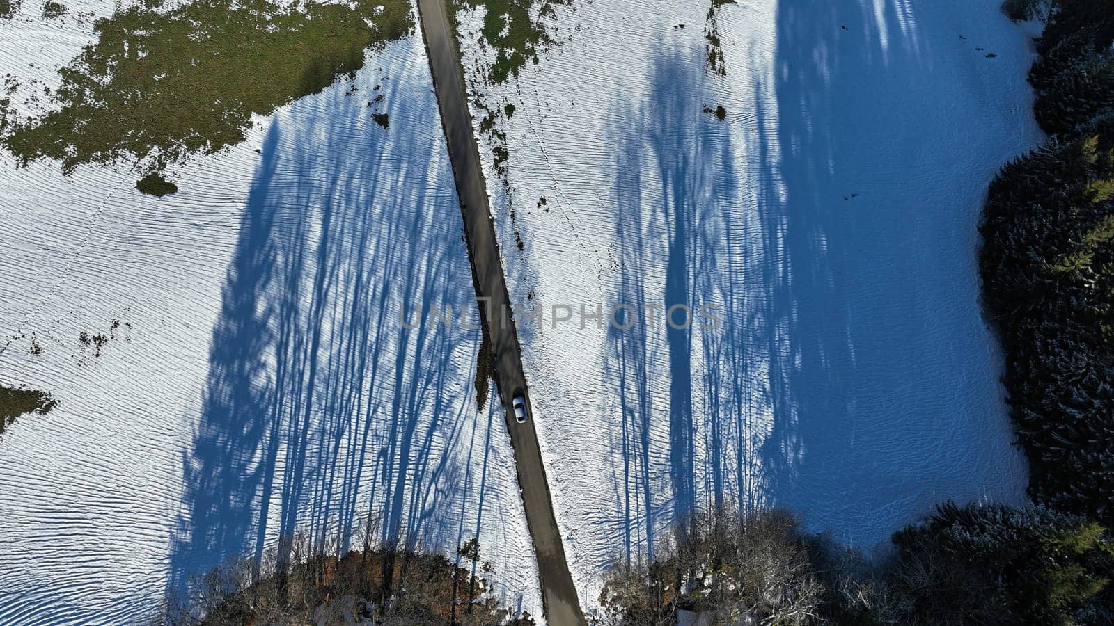Aerial shot with drone of snowy landscape with shadow and road with white car