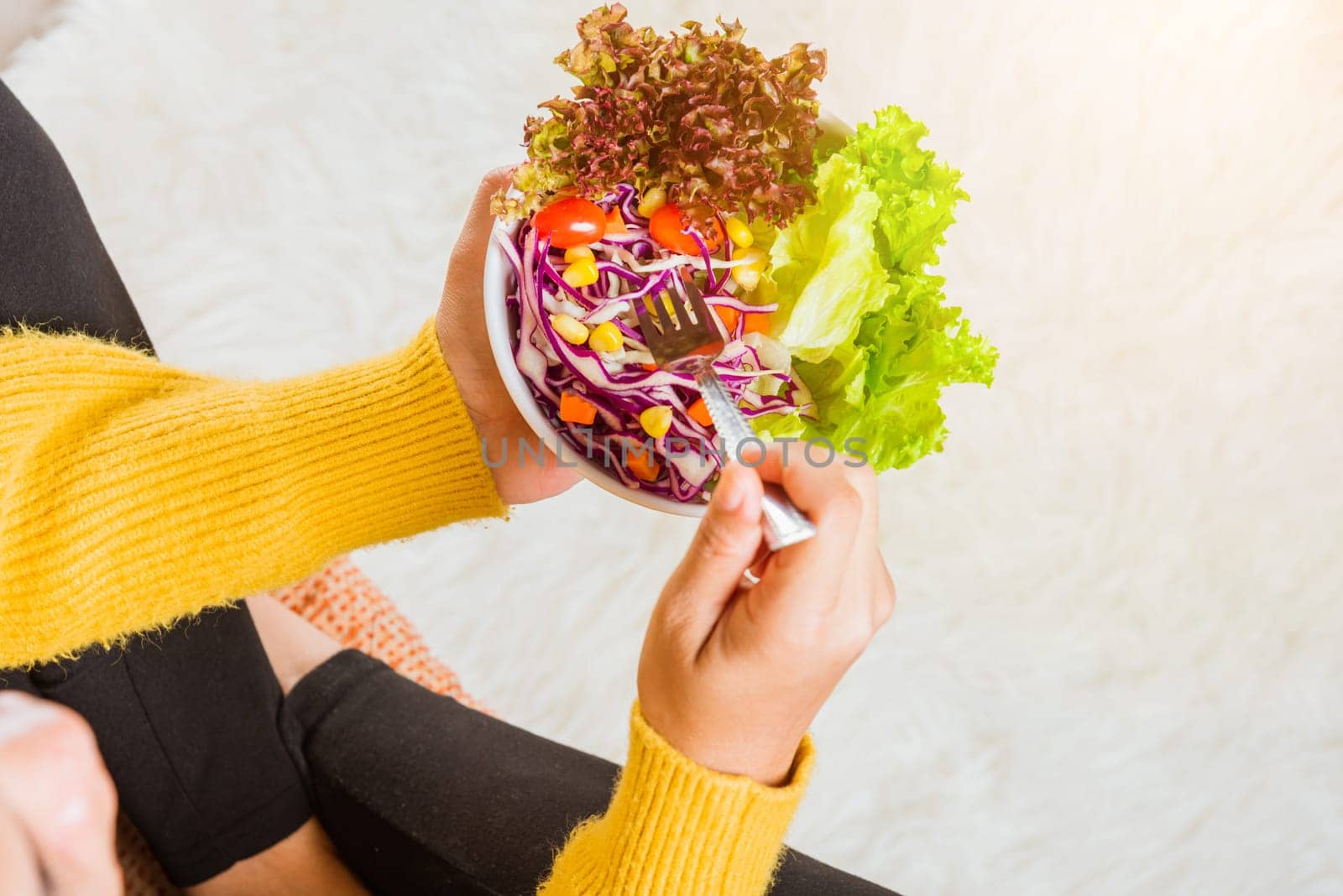 Top view of female hands holding bowl with green lettuce salad on legs, a young woman eating fresh salad meal vegetarian spinach in a bowl, Clean detox healthy food concept