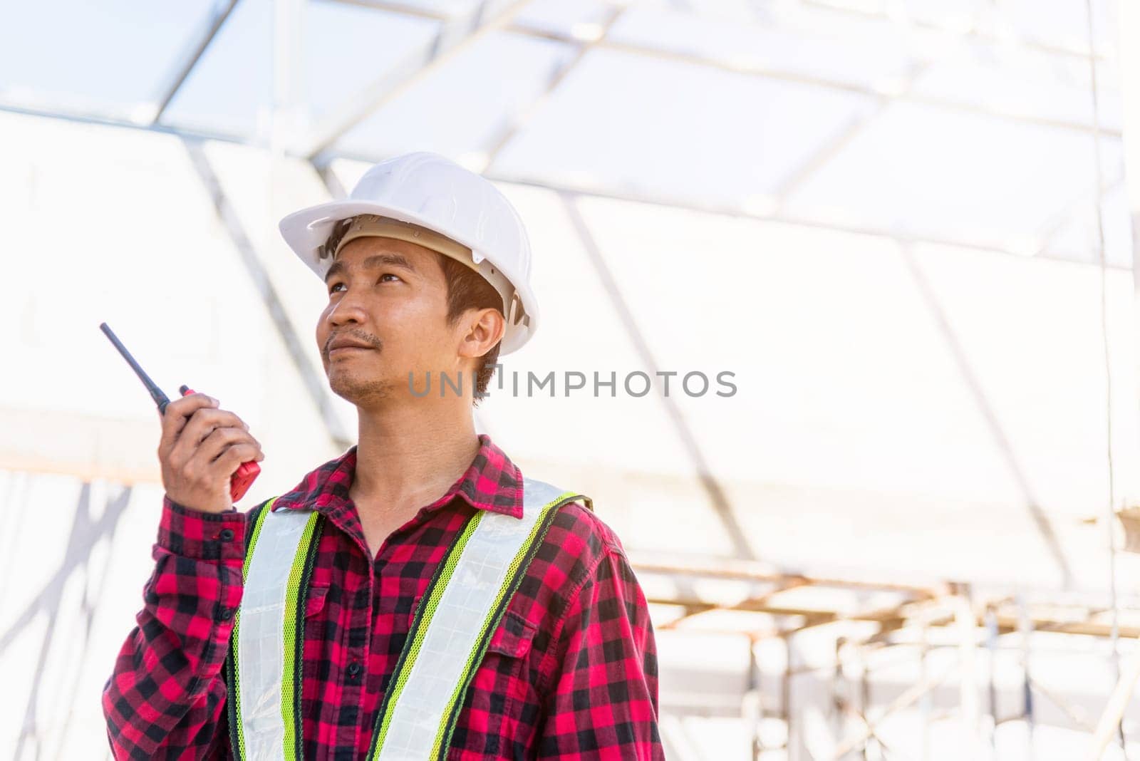 Asian engineer foreman architect worker man working at building construction site talking with radio, engineering hold radio discuss operate and control worker employee to building construction