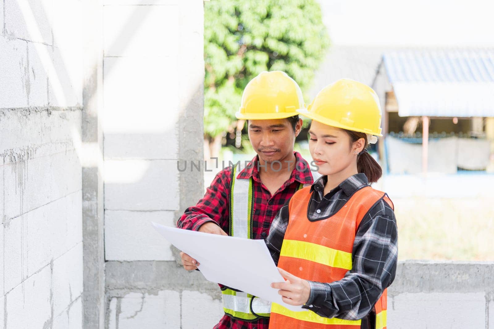Architect and client discussing the plan with blueprint of the building at construction site. Asian engineer foreman worker man and woman working talking and checking on draw paper to checking project