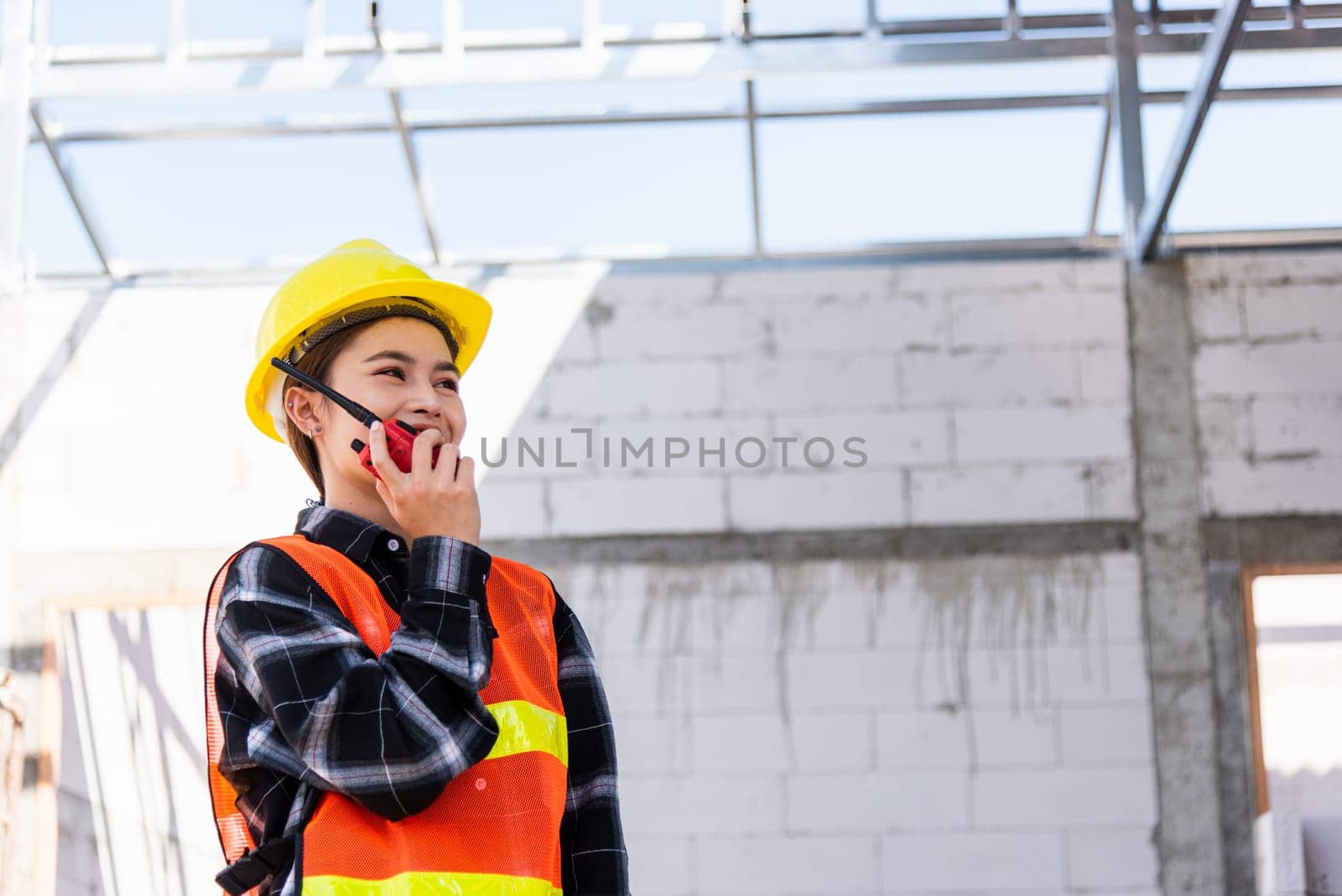 Asian engineer foreman architect worker woman working at building construction site talking with radio, engineering hold radio discuss operate and control worker employee to building construction