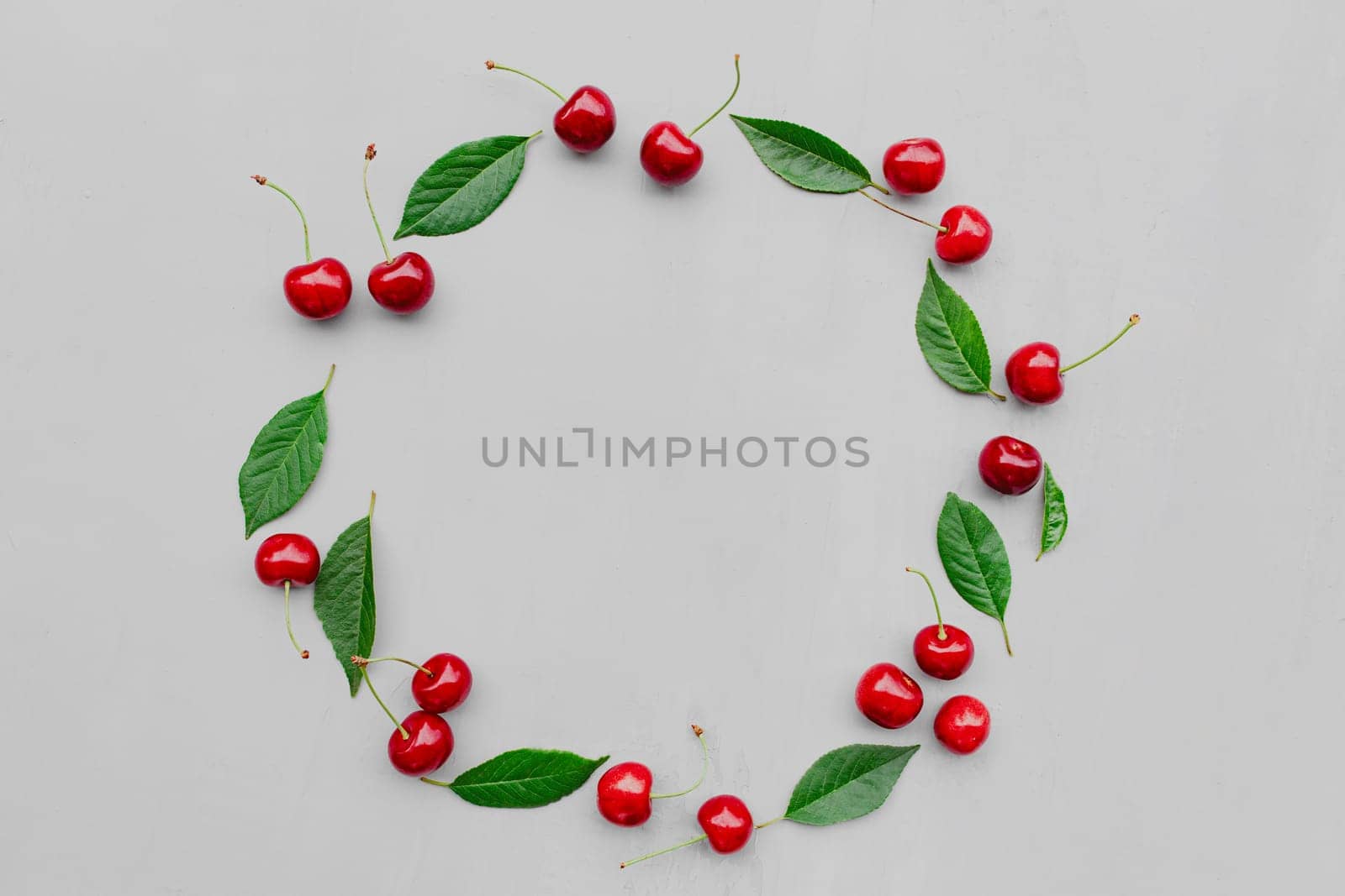 Gray concrete flat lay with big sweet cherries on table background. Top view on huge, massive organic cherry berries with leaves in form of empty circle shape. Copy space area for advertisement text