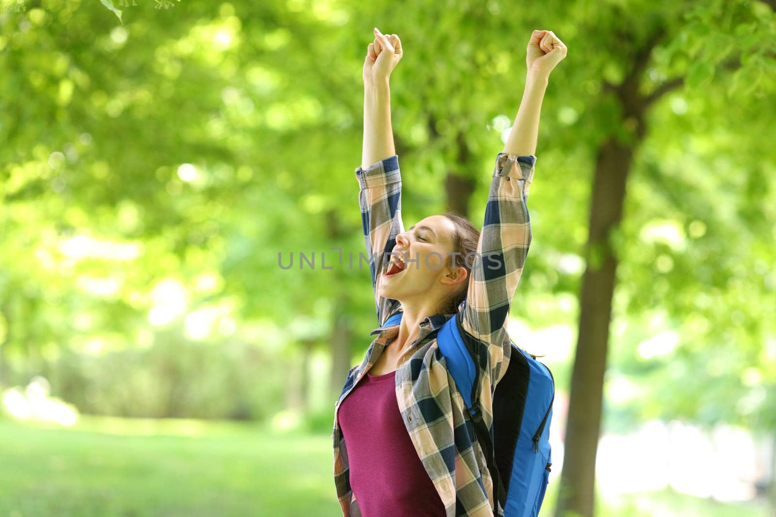 Excited student raising arms celebrating success in a park