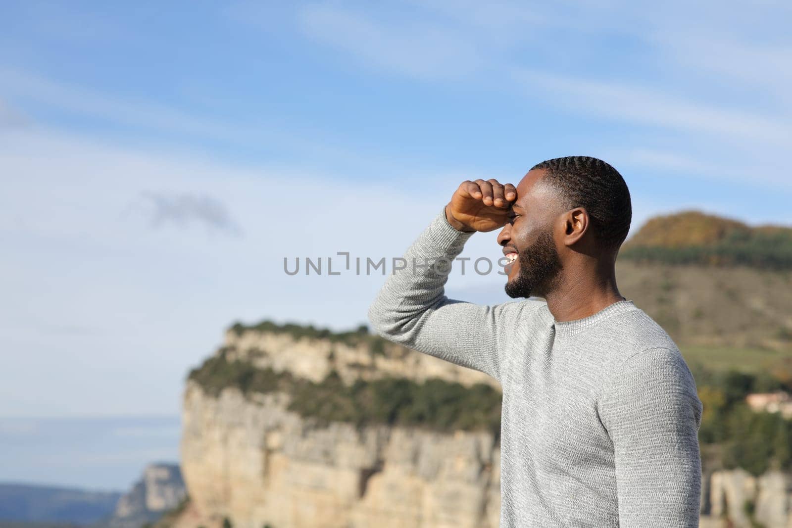 Happy man with black skin searching looking away protecting from sun with his hand in the mountain