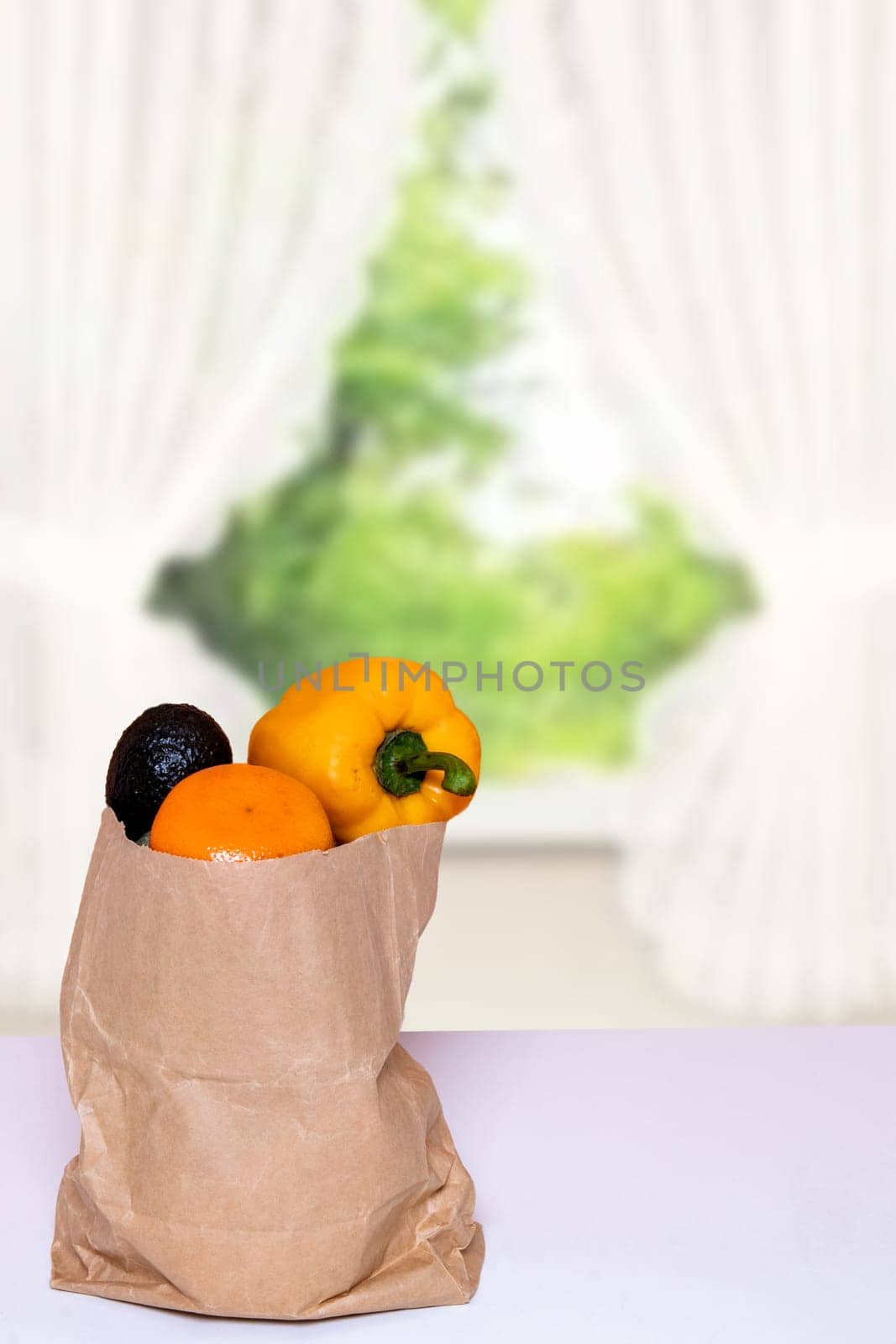 Closeup of a brown paper shopping bag with fresh vegetables on table over blurred abstrract curtain background. Space for product display montage. Concept of strengthening the immune system.