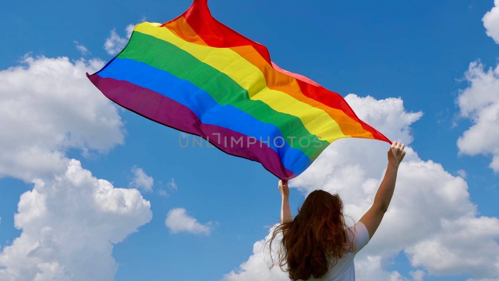 Bisexual, lesbian, woman, transgender holds LGBT flag in the background of blue sky with clouds on a sunny day and celebrates Transgender Remembrance Day, Bisexuality or Coming Out Day