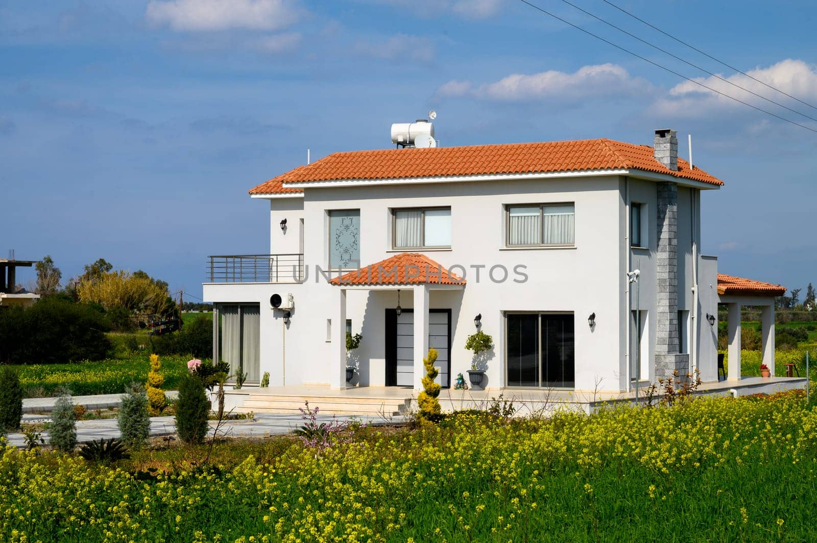 Bright, spacious home nestled in lush greenery and vibrant flowers under a clear blue sky on a warm day.