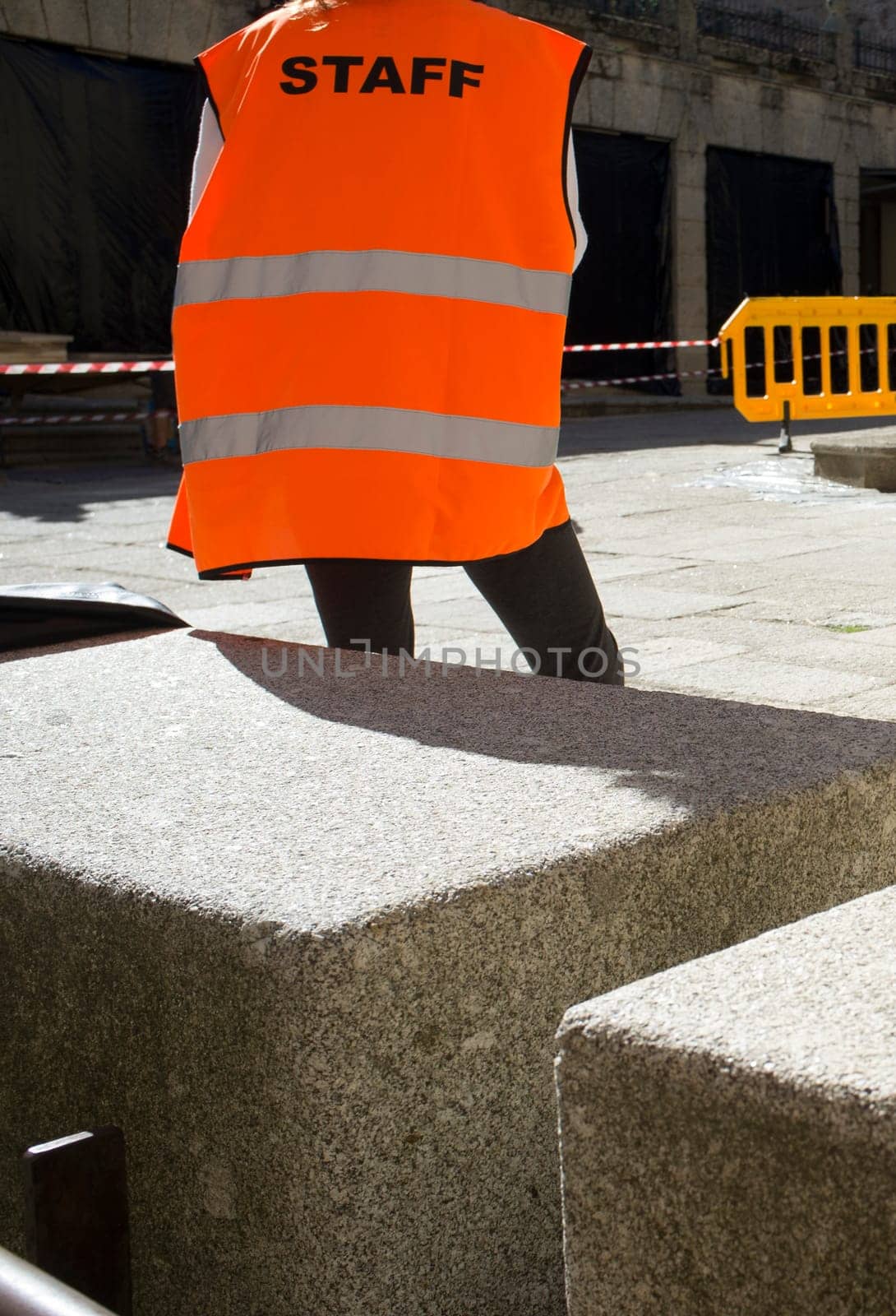 Staff worker watching security area marked by mobile fence and cones and tape