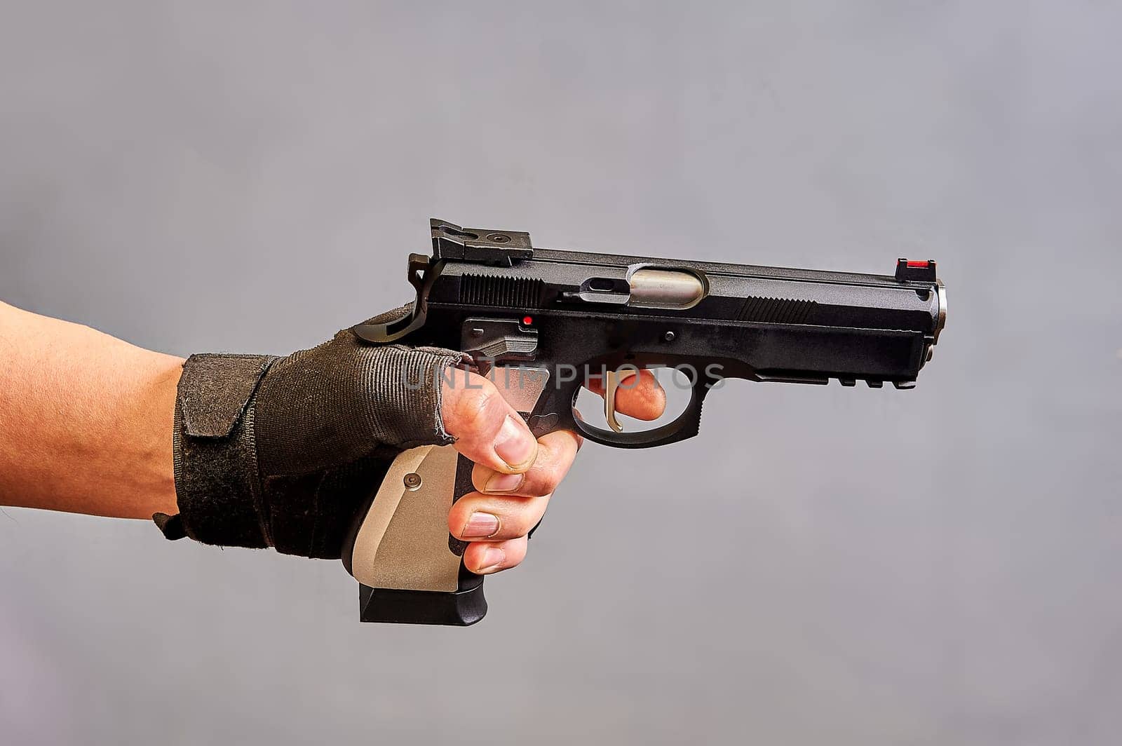 A man's hand holds a black pistol in his hand on a gray background. High quality photo