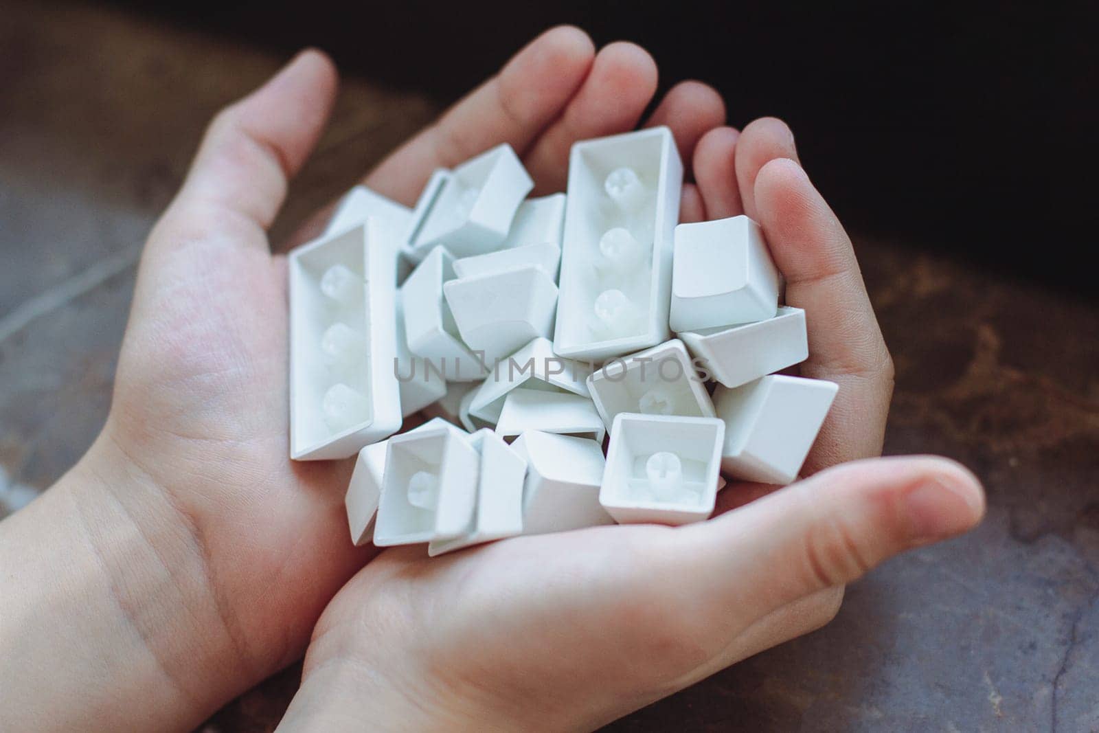 top view closeup of Caucasian child hands holding many pbt keycaps of a white mechanical keyboard in natural lighting