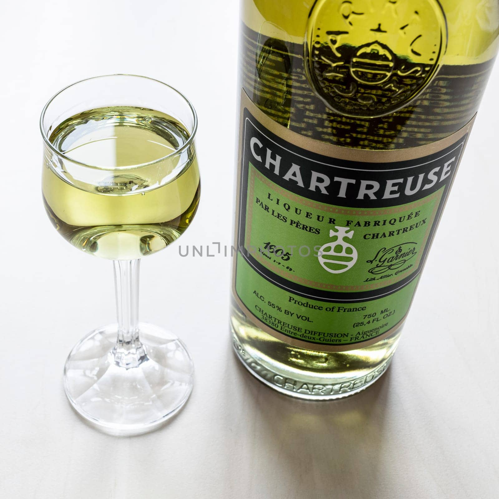Moscow, Russia - February 3, 2022: liqueur glass and bottle of green Chartreuse liqueur close up on pale table. The liqueur has been made by the Carthusian Monks n France since 1737