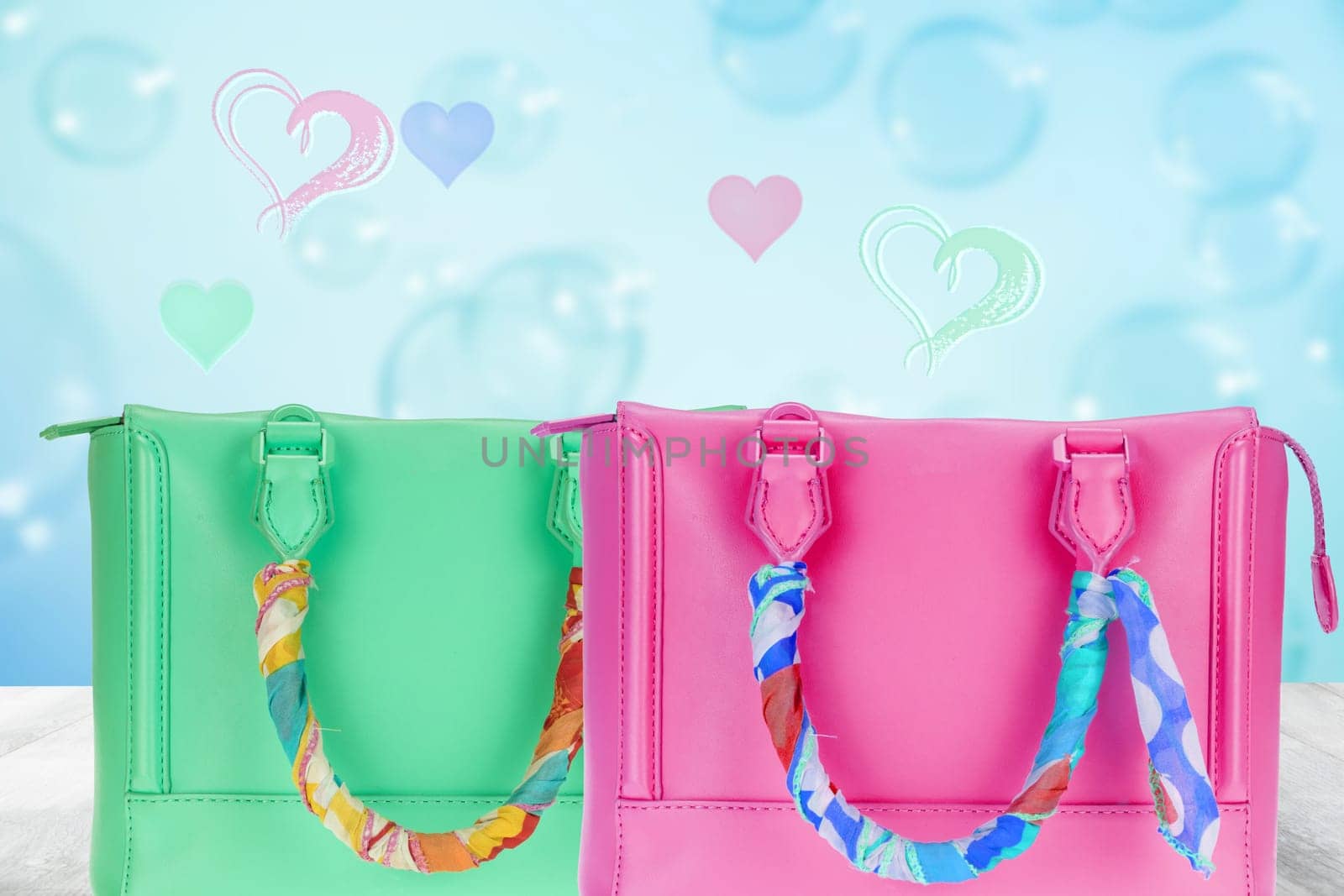 Happy Valentines or Mothers Day template. A beautiful green and a pink women's handbag decorated with a colourful cloth on the table over abstract blue heart background.