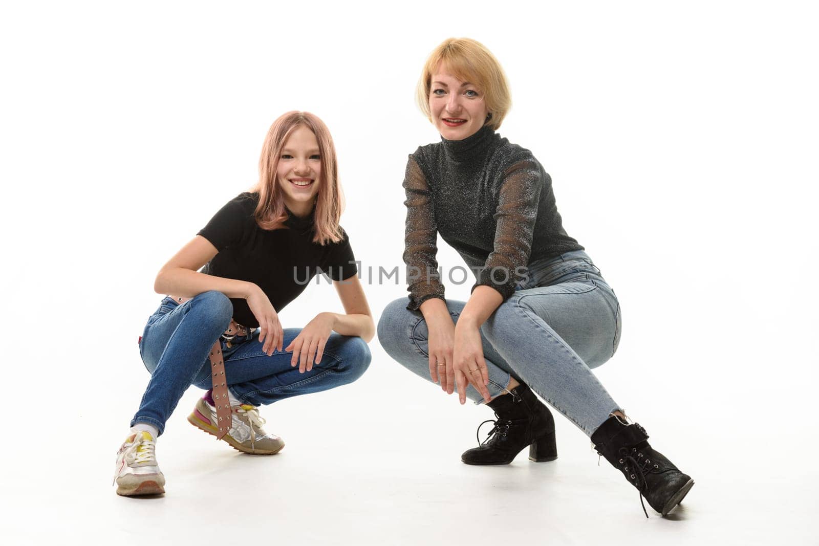 Mother and teenage daughter sat on their knees and cheerfully look into the frame