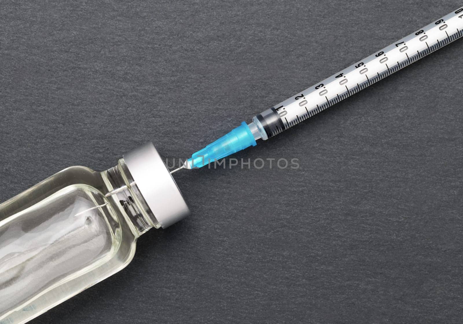 Liquid medicine in vials and injection syringe on dark gray background