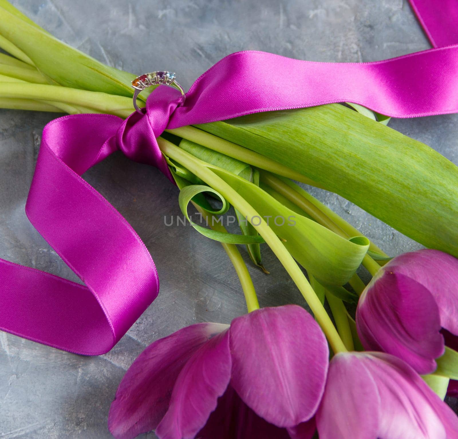 Bouquet of purple tulips with tied engagement or wedding ring and handwritten I LOVE YOU card in envelope on grey table. Valentine's Day celebration, marriage proposal, romantic holiday concept