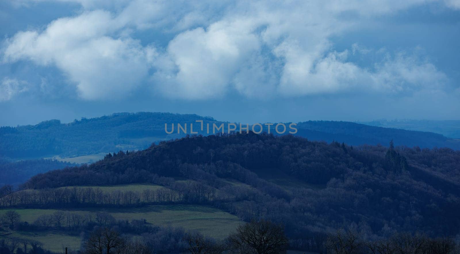 Blue landscape with hill and forest and cloudy sky