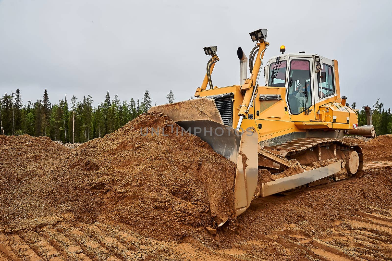 A yellow tractor levels the site with sand. High quality photo