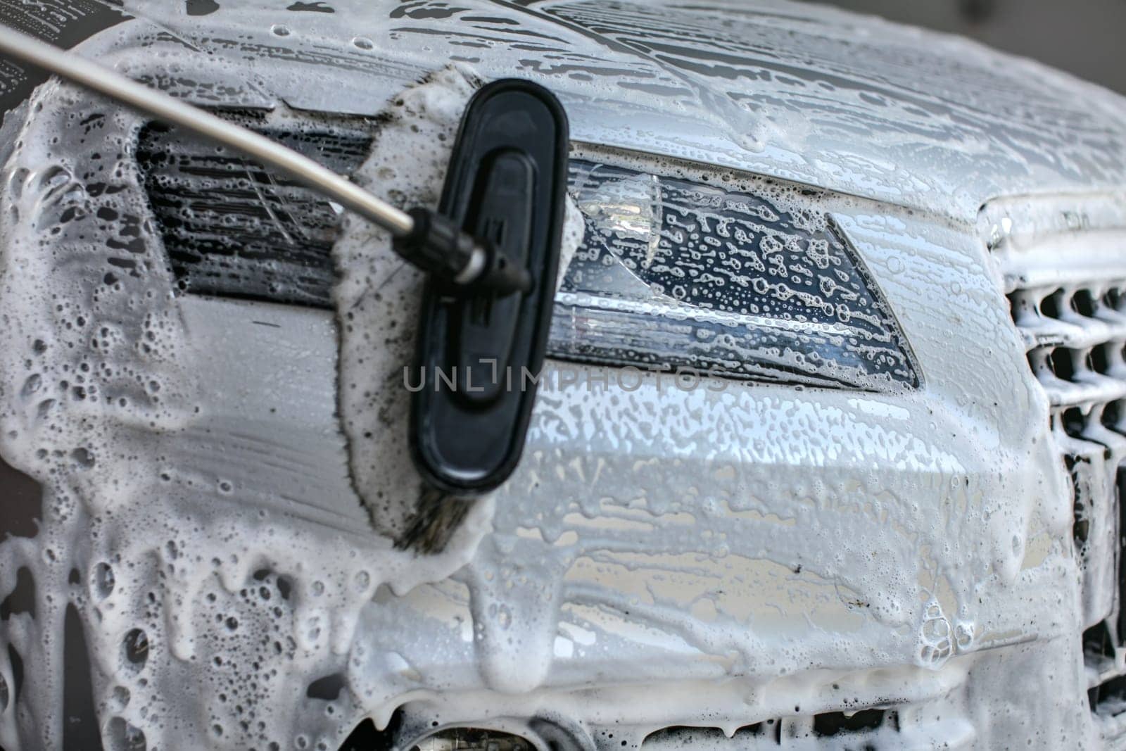 Front light of silver car washed in self service carwash. Brush leaving strokes in shampoo and foam