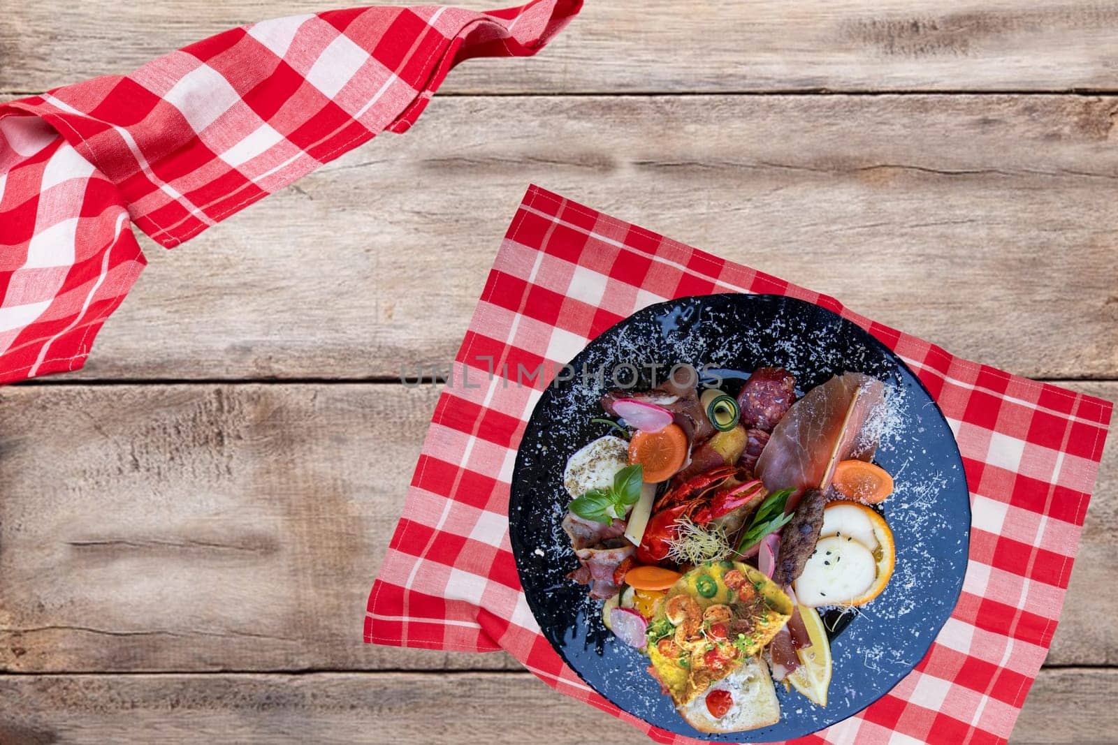 Traditional italien food. Closeup of mixed mediterranean appetizers or antipasto and tapas with ham vegetables and cancer on a black plate on a rustic wooden table. Top view.