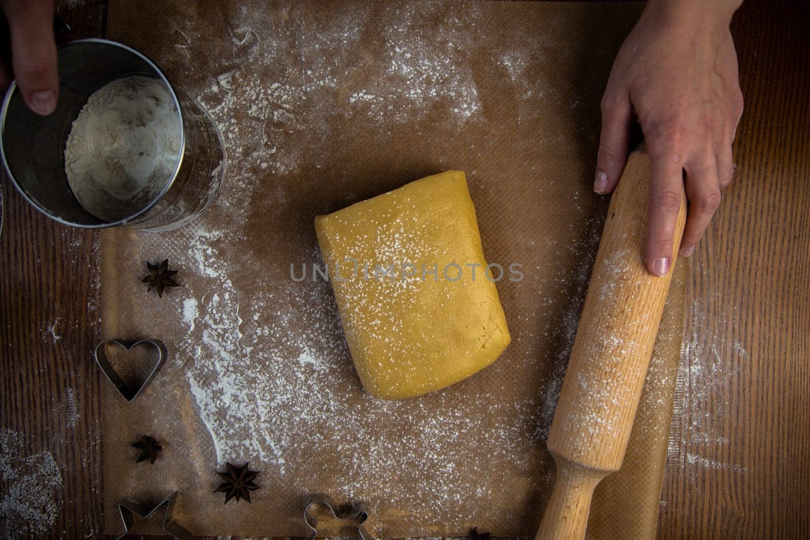 A rectangle of dough lies on baking parchment, a rolling pin and cookie cutters are lying next to it, everything is strewn with flour, a cook is standing in the background and holding a rolling pin and flour powder. High quality photo