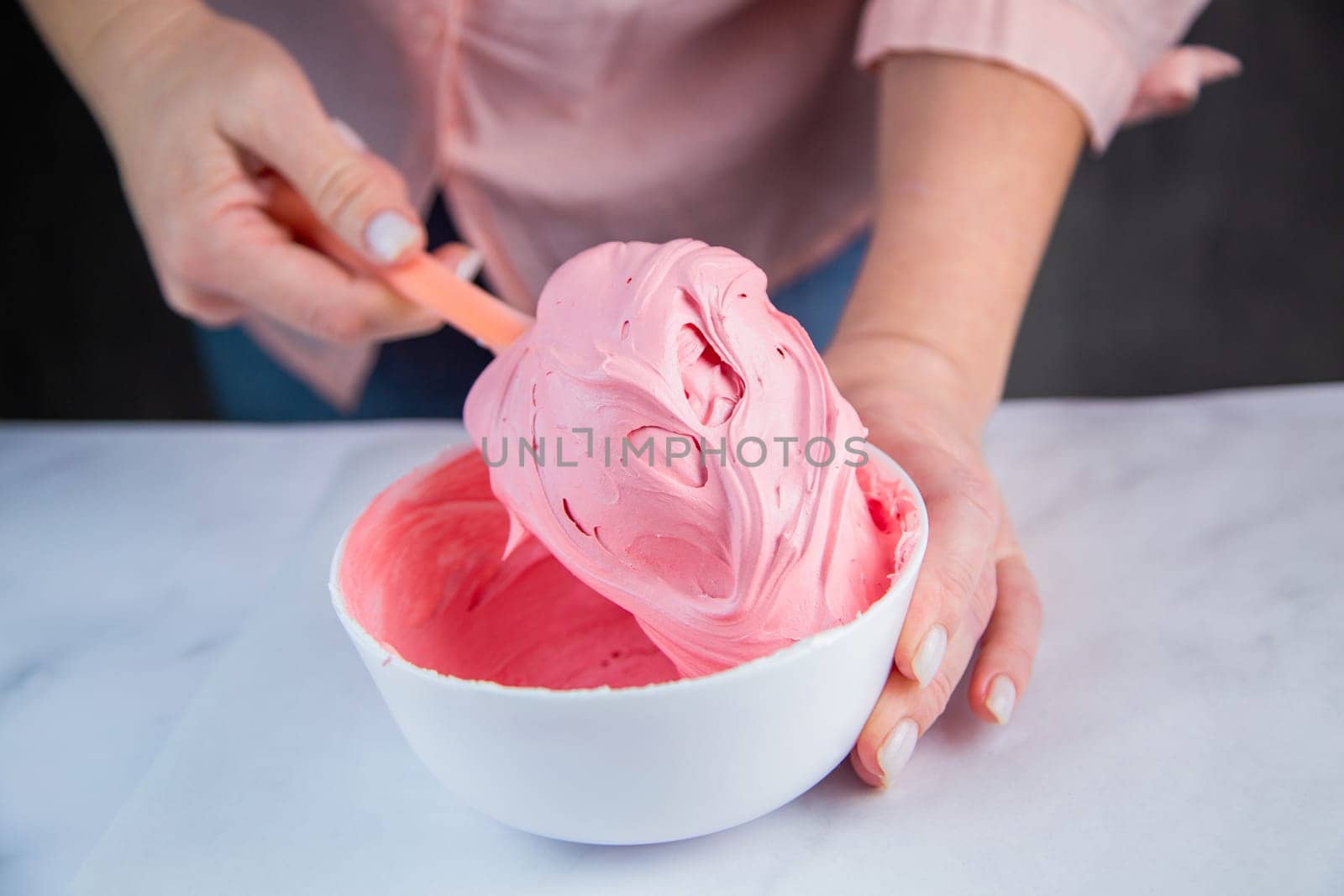 Pink confectionary meringue marengo is mixed in a white bowl on a white marble background by the hands of a pastry chef. High quality photo