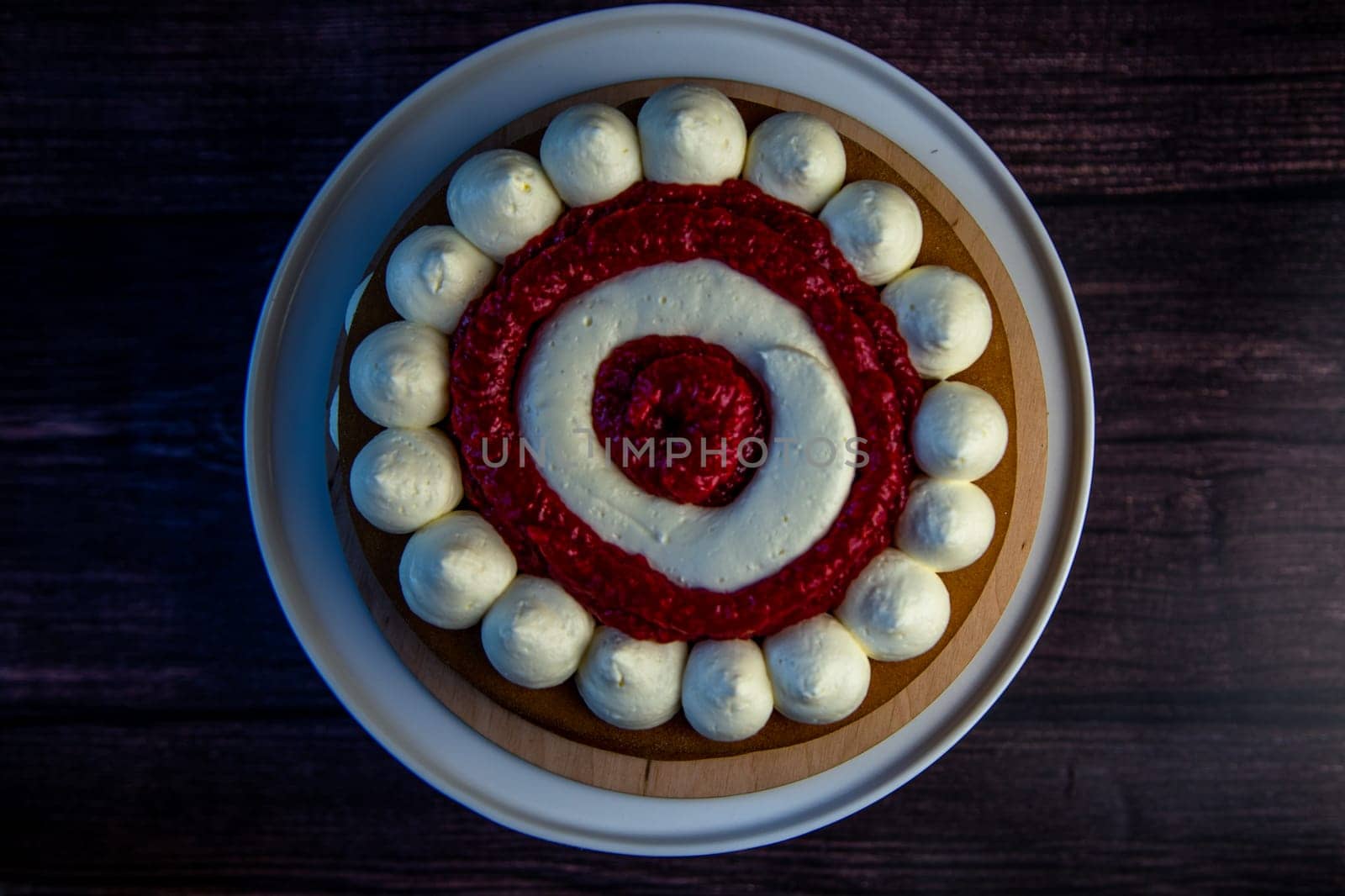 A cake with circles of white cream alternating with raspberry jam on a dark background, top view, close-up. High quality photo