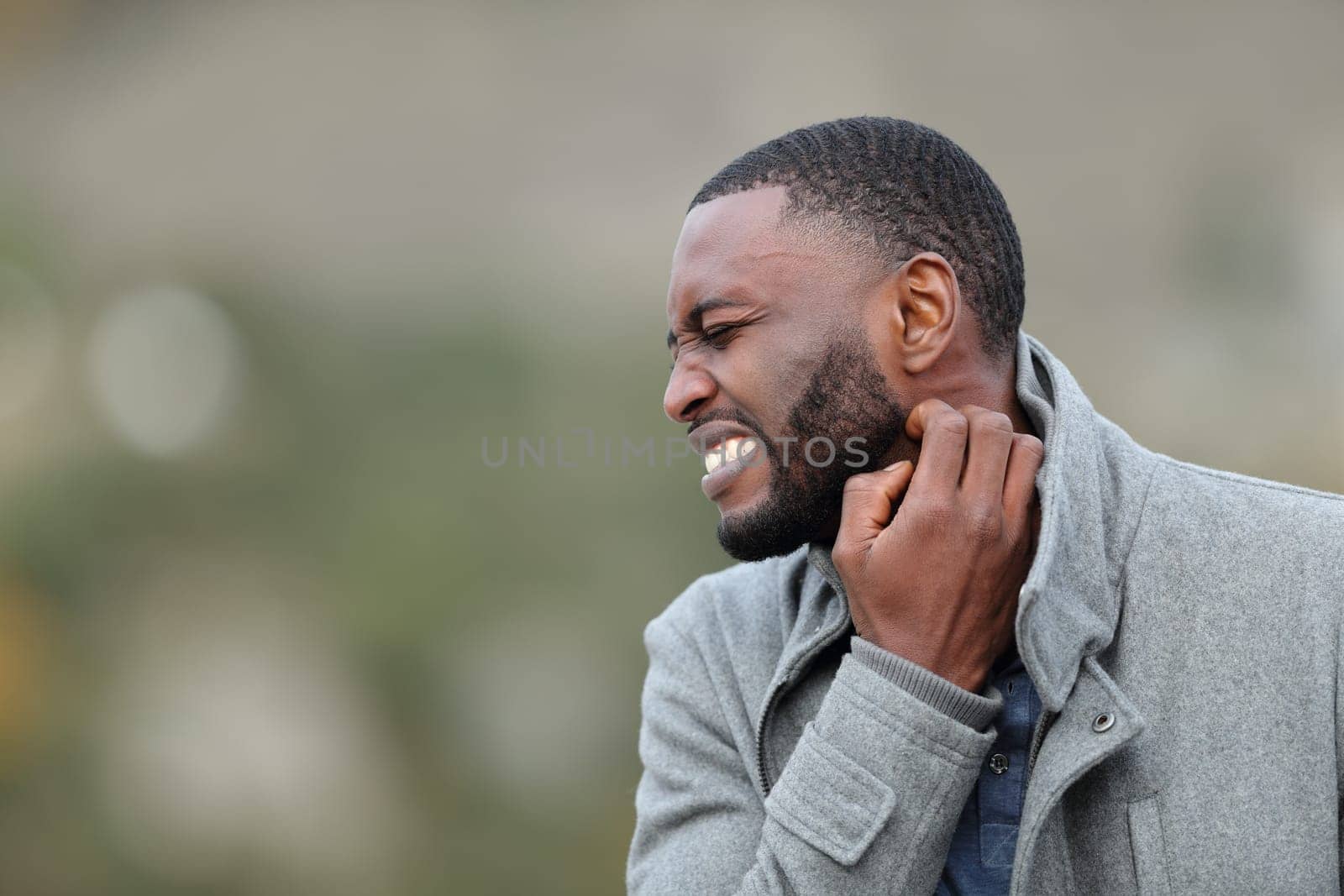 Stressed man with black skin scratching itchy neck in winter in a park