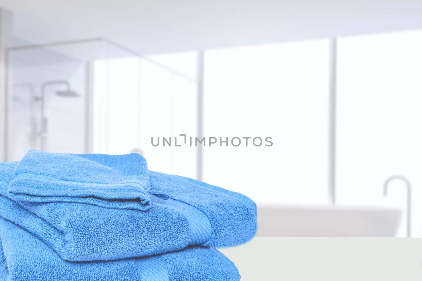 Table top on towels background. Closeup of a stack or pile of blue soft terry bath towels at a bright table against abstract blurred bathroom background. Space.