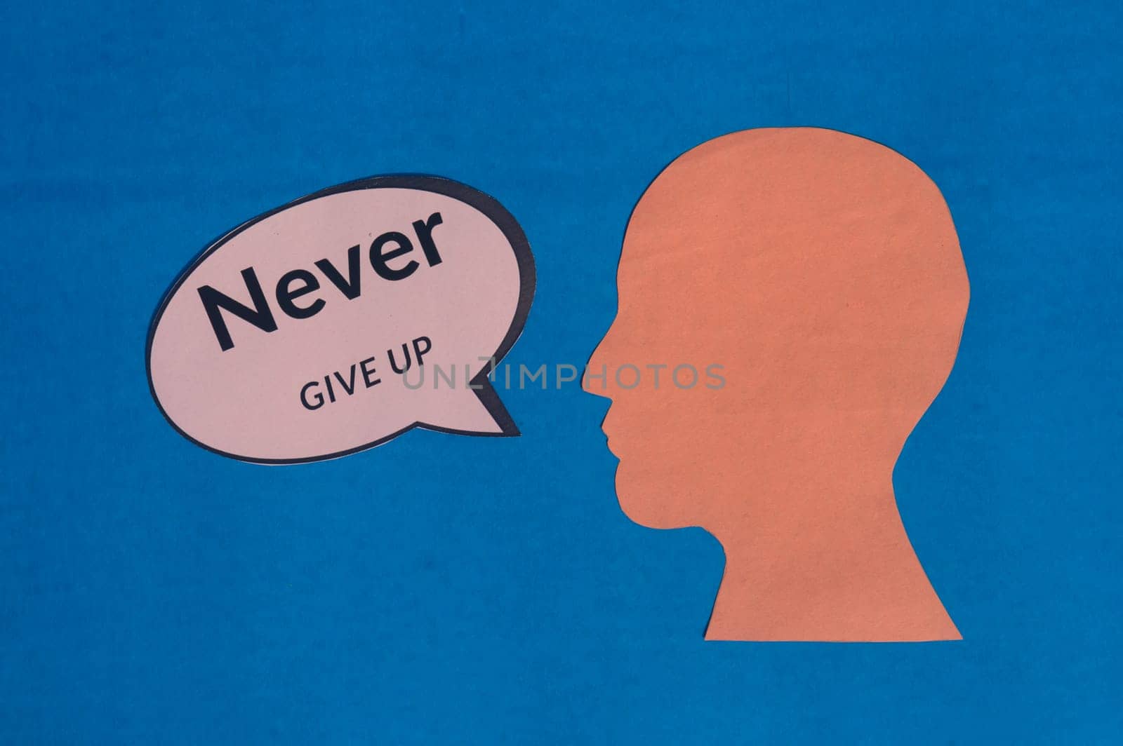 Paper human face with motivation text on speech bubble isolated on blue background. Conceptual image shows believing in yourself and willingness to accept failure to achieve goals
